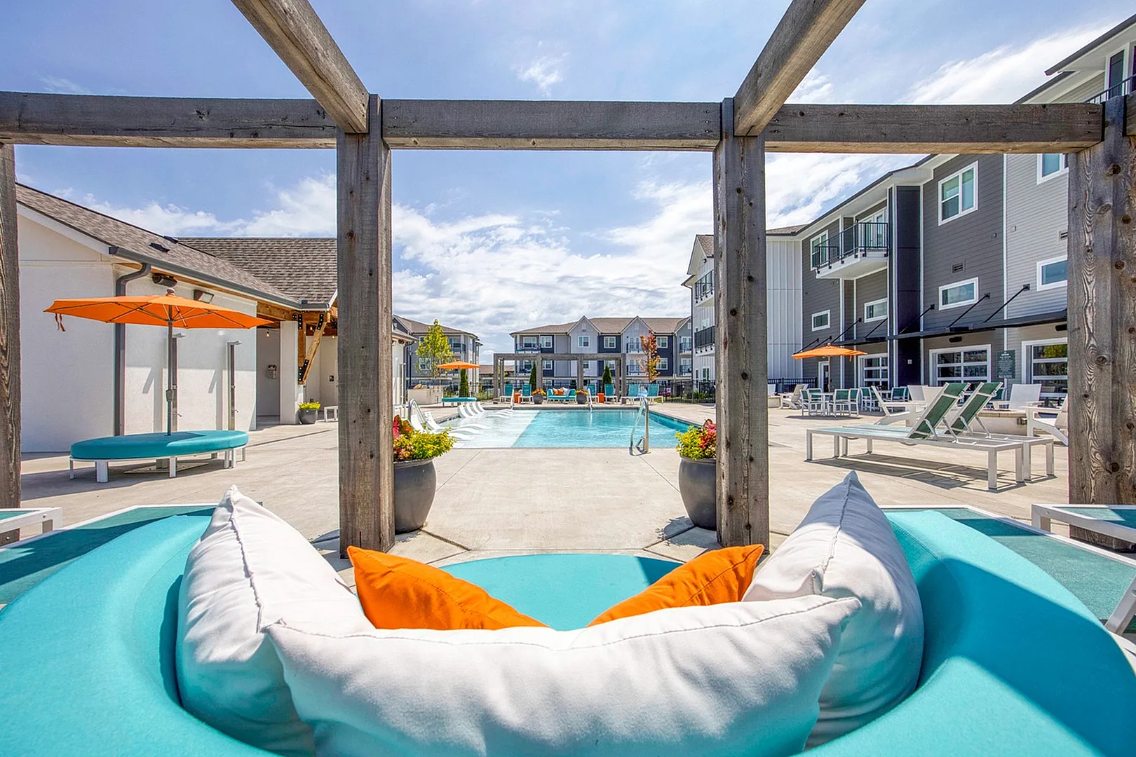 Luxurious apartment complex featuring a stunning outdoor pool area with vibrant seating, orange umbrellas, and elegant modern architecture.