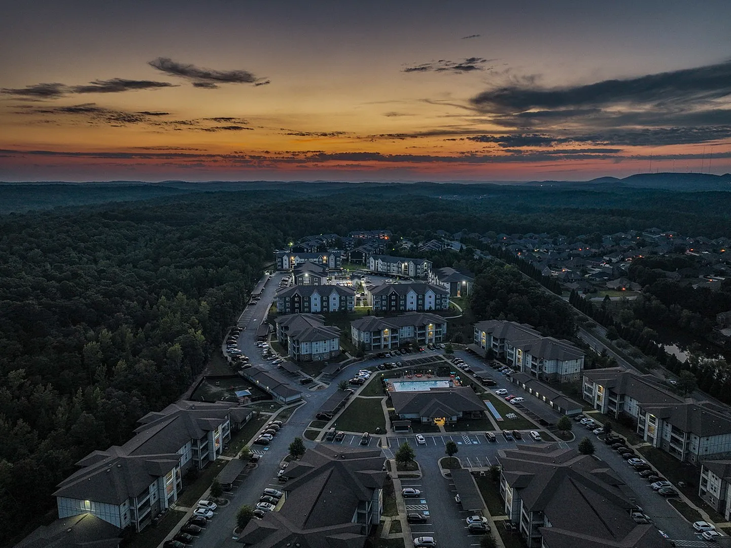 Stunning aerial view of modern apartment complex nestled amid lush greenery at sunset, highlighting a serene and vibrant community setting.