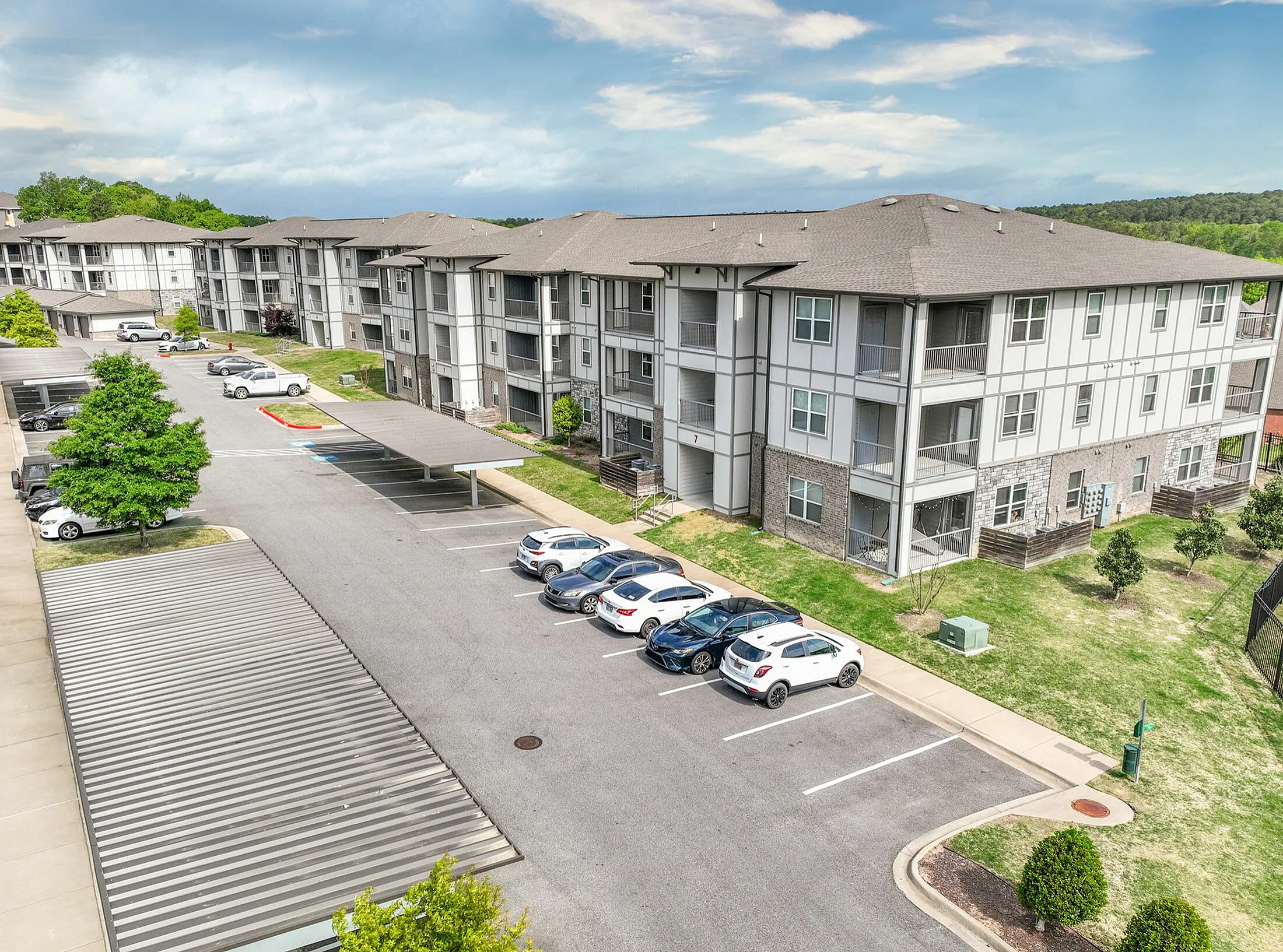 Modern apartment complex with spacious parking, surrounded by lush greenery and clear blue skies.