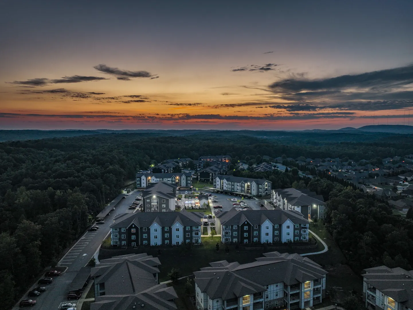 Enchanting evening aerial view of a serene apartment complex nestled in lush greenery, highlighted by a breathtaking sunset sky.