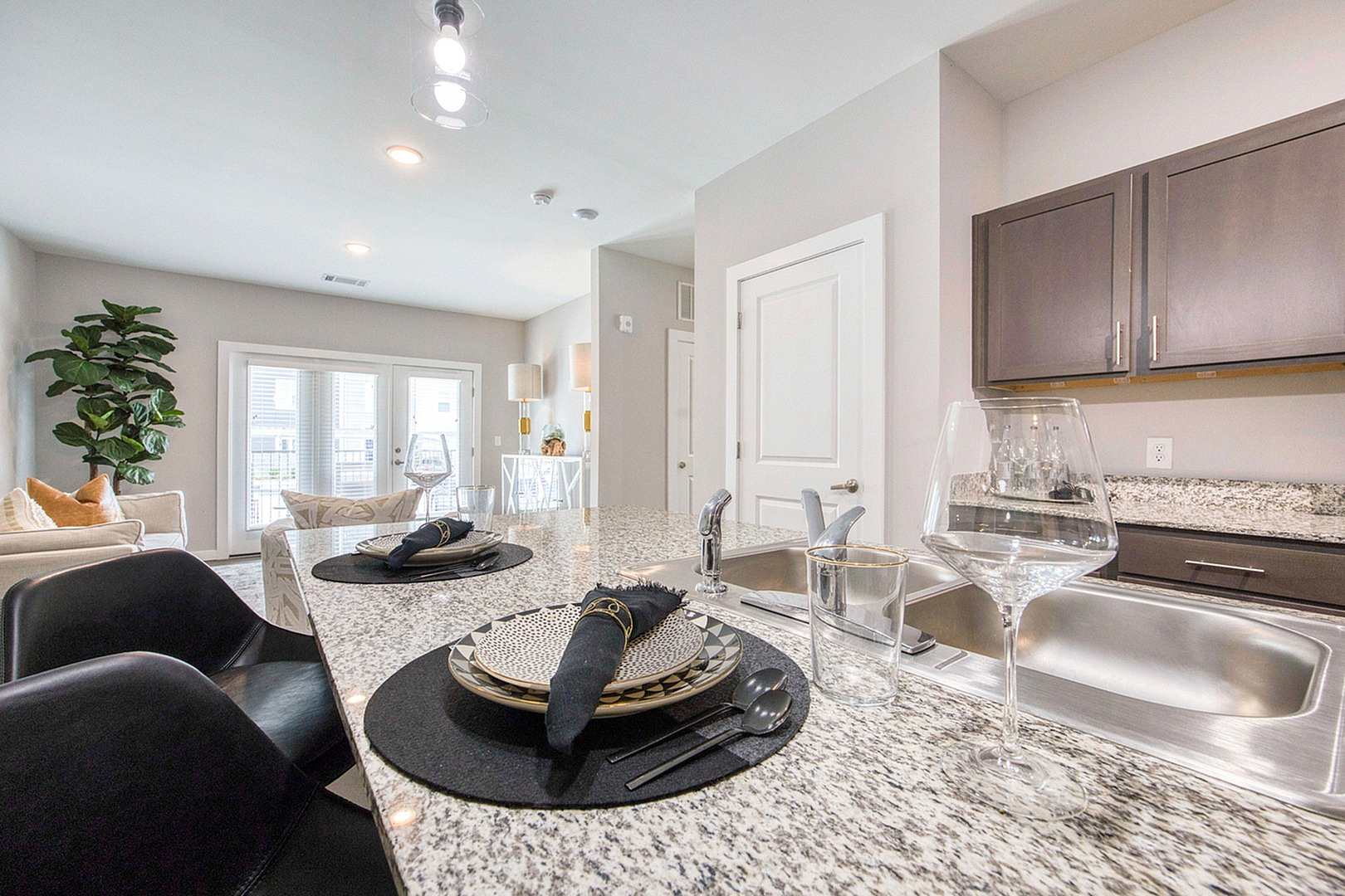 Elegant modern kitchen with granite countertops and set dining for two, opening to a bright, spacious living area with stylish decor and large windows.