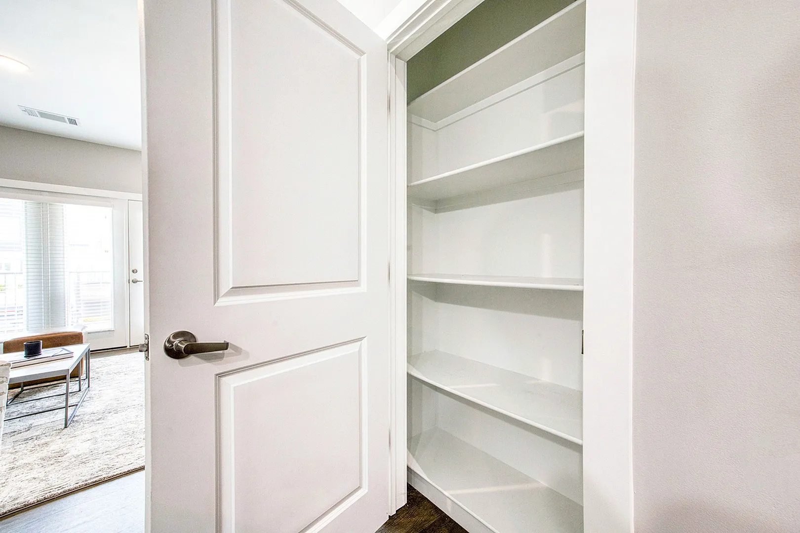 Bright and inviting open door revealing a spacious closet with built-in shelving, perfect for versatile storage solutions in a modern apartment.
