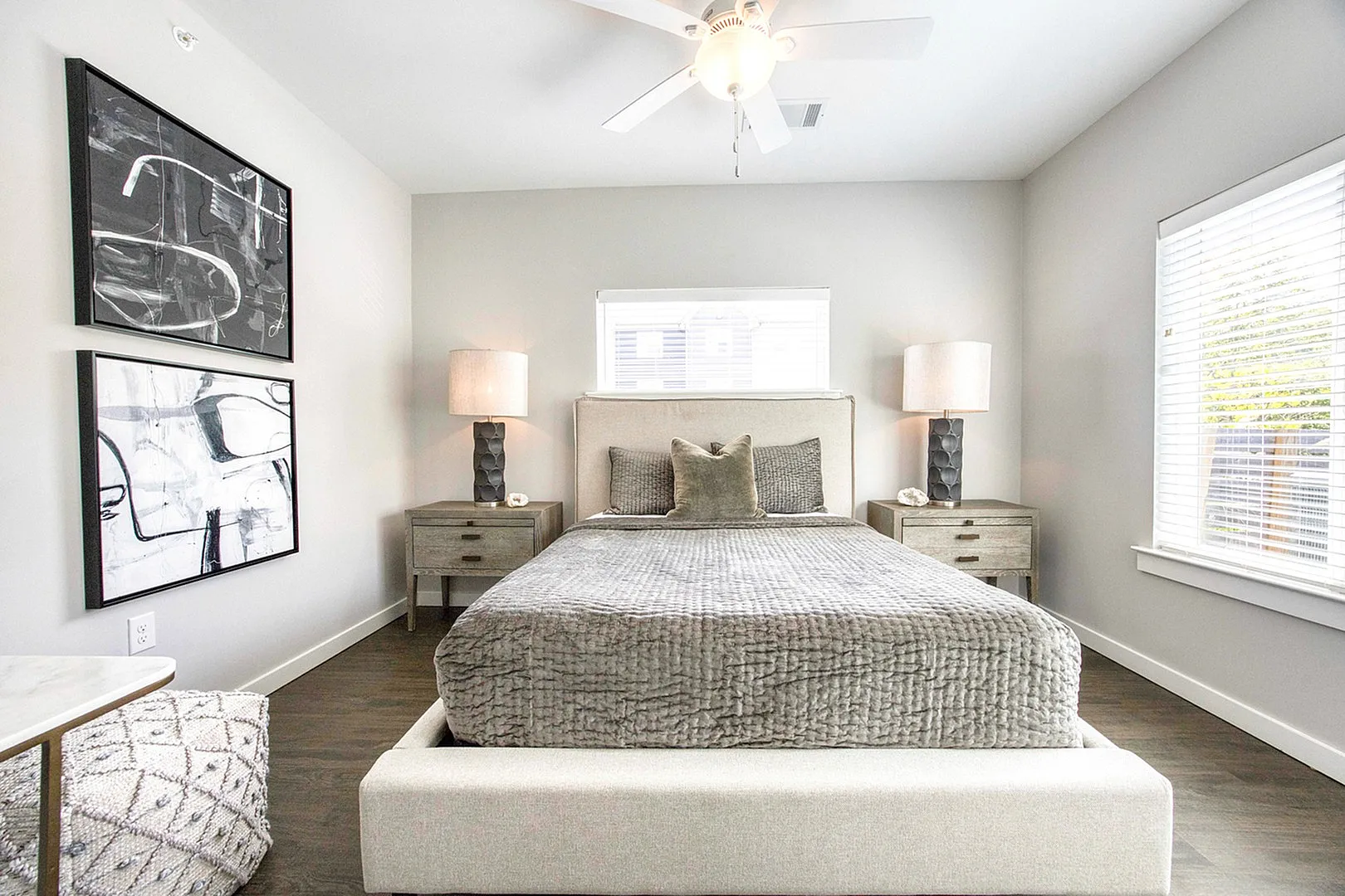 Inviting bedroom with elegant decor, featuring a plush gray bed, artistic wall paintings, and abundant natural light.