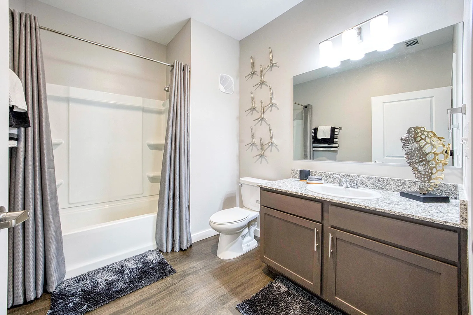 Elegant bathroom featuring a modern vanity with granite countertop, sleek shower with gray curtains, and stylish decor on the walls, offering a luxurious and serene atmosphere.
