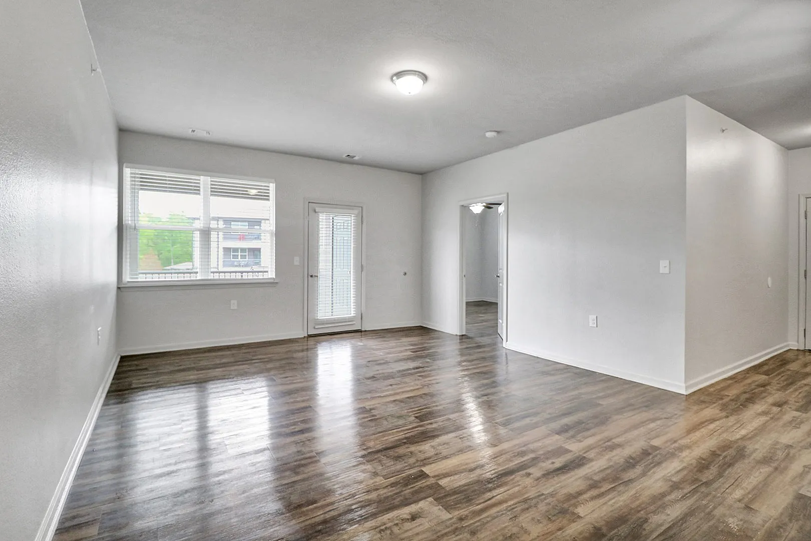 Bright and spacious living area with elegant wood flooring, large window, and access to a private balcony.