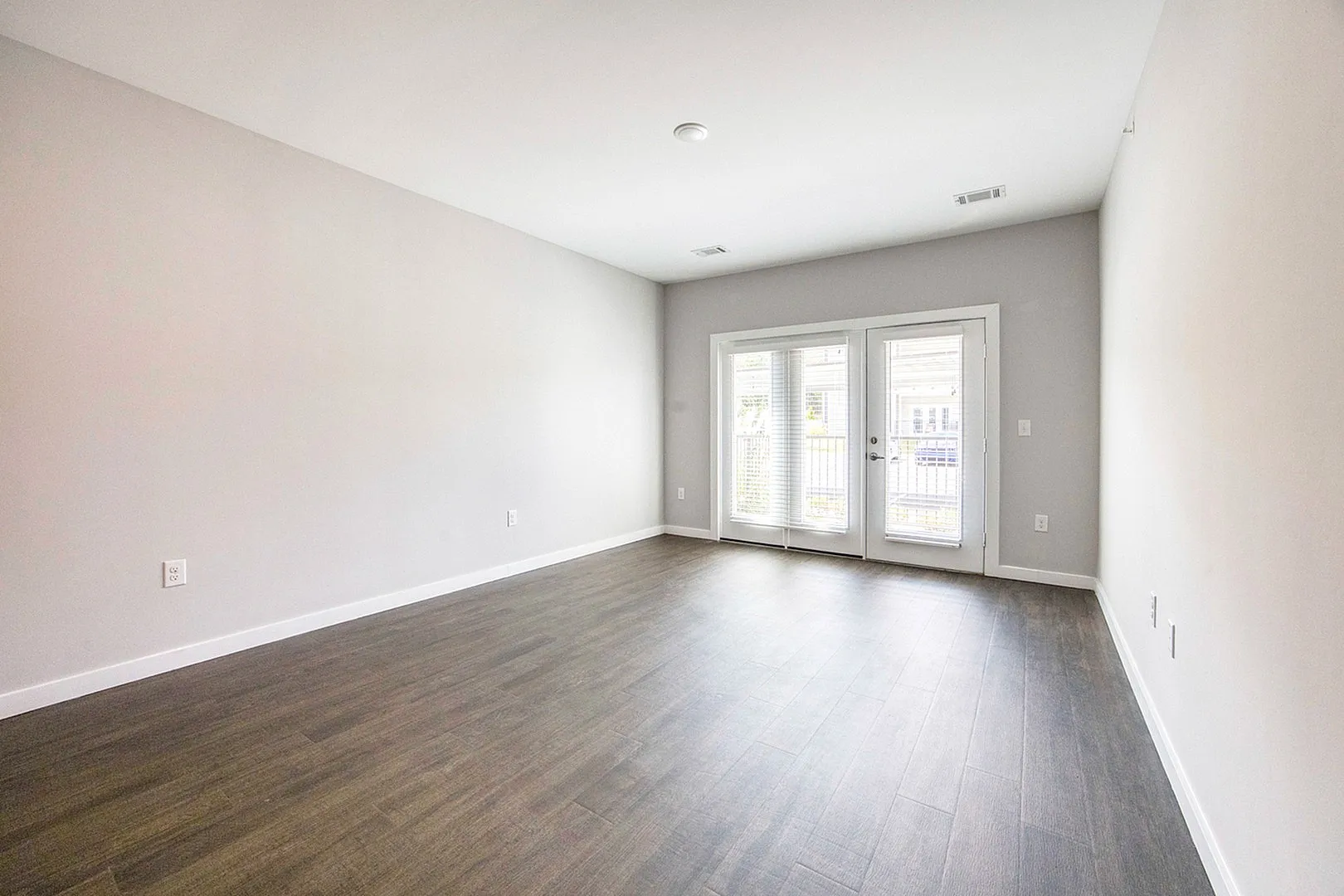 Bright, open living space with elegant hardwood flooring and double French doors leading to a sunlit patio.