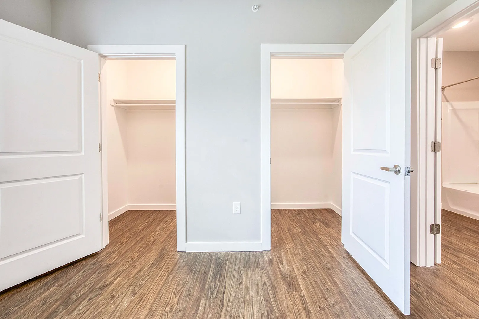 Bright and modern apartment closet space with sleek wooden flooring, ample light, and elegant white doors.