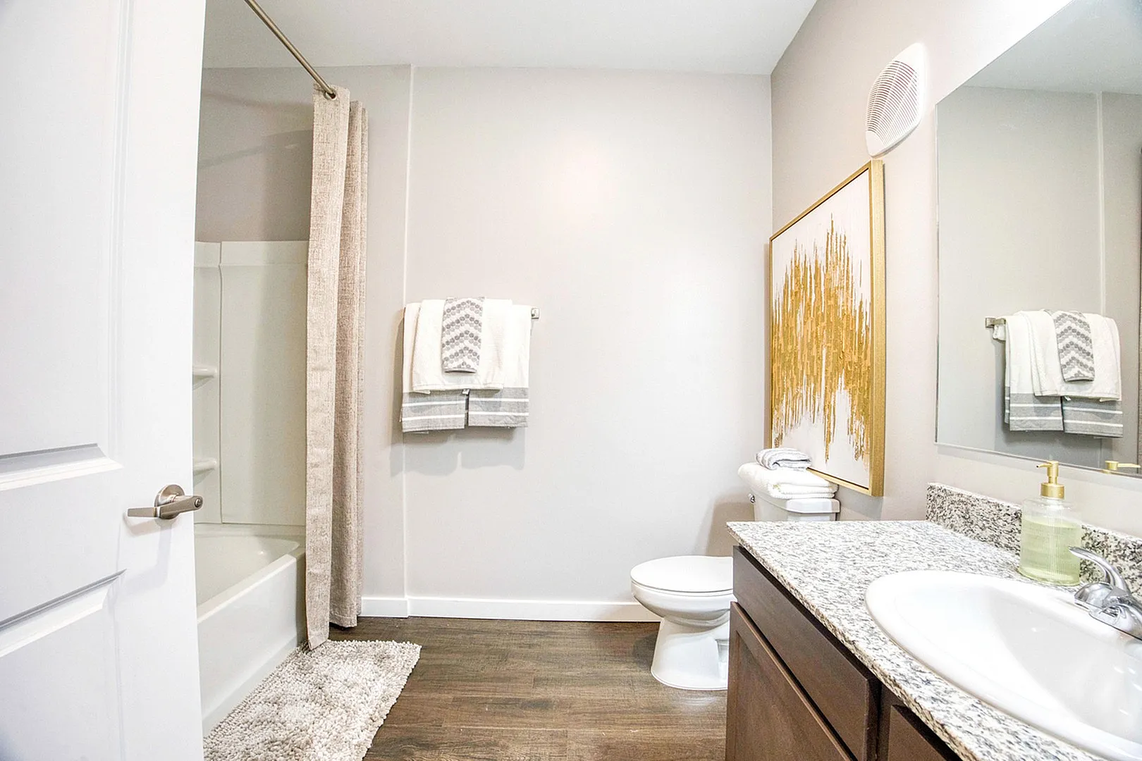 Elegant bathroom with modern design featuring granite countertop, wooden cabinetry, and stylish wall art. Bright and inviting space with a shower-tub combination and plush towels.