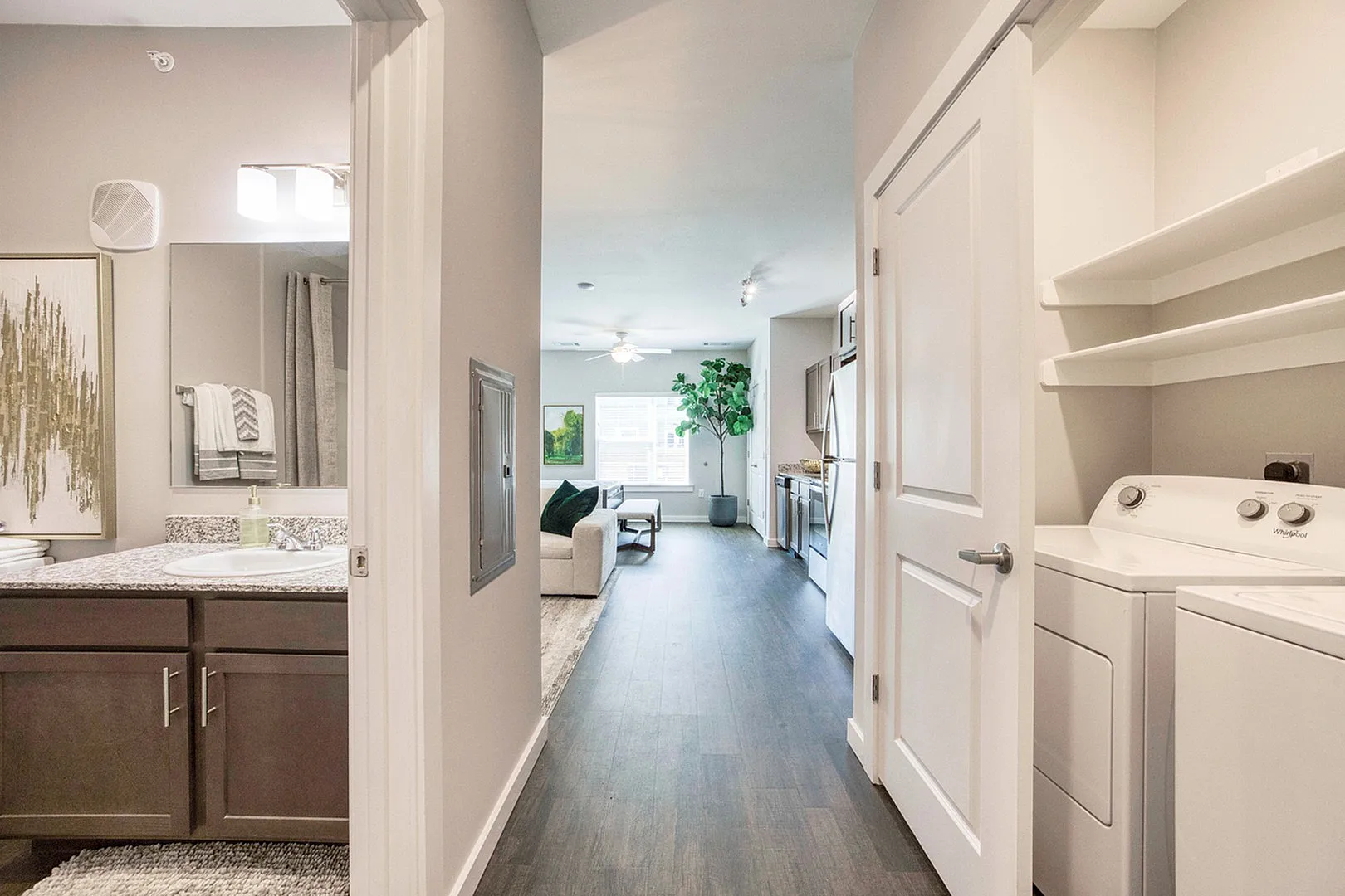 Inviting apartment hallway with dark wood flooring, showcasing a modern bathroom, cozy living area, and in-unit laundry.