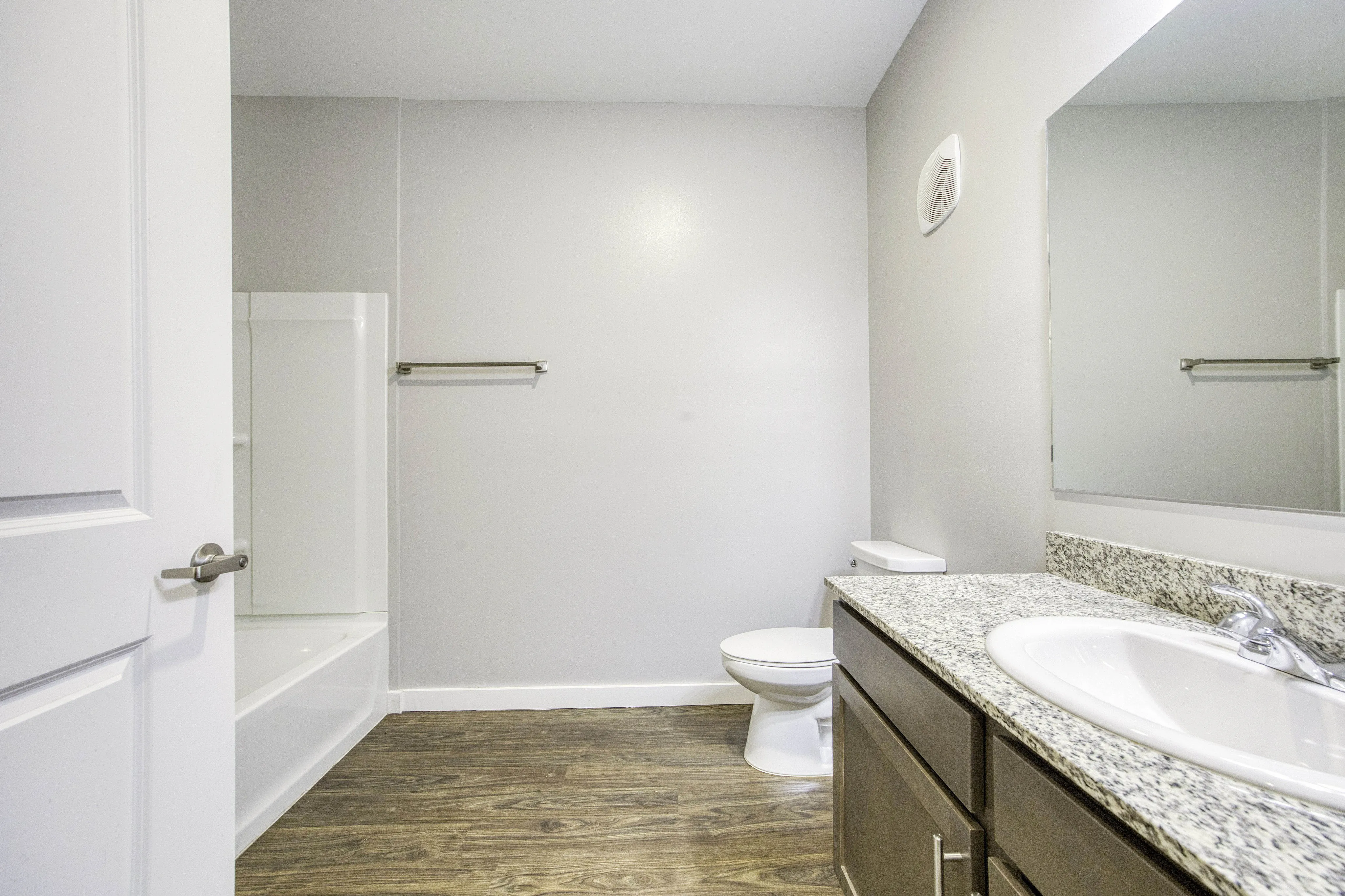 Bright, modern bathroom featuring sleek granite countertop, elegant wooden flooring, and inviting bathtub.