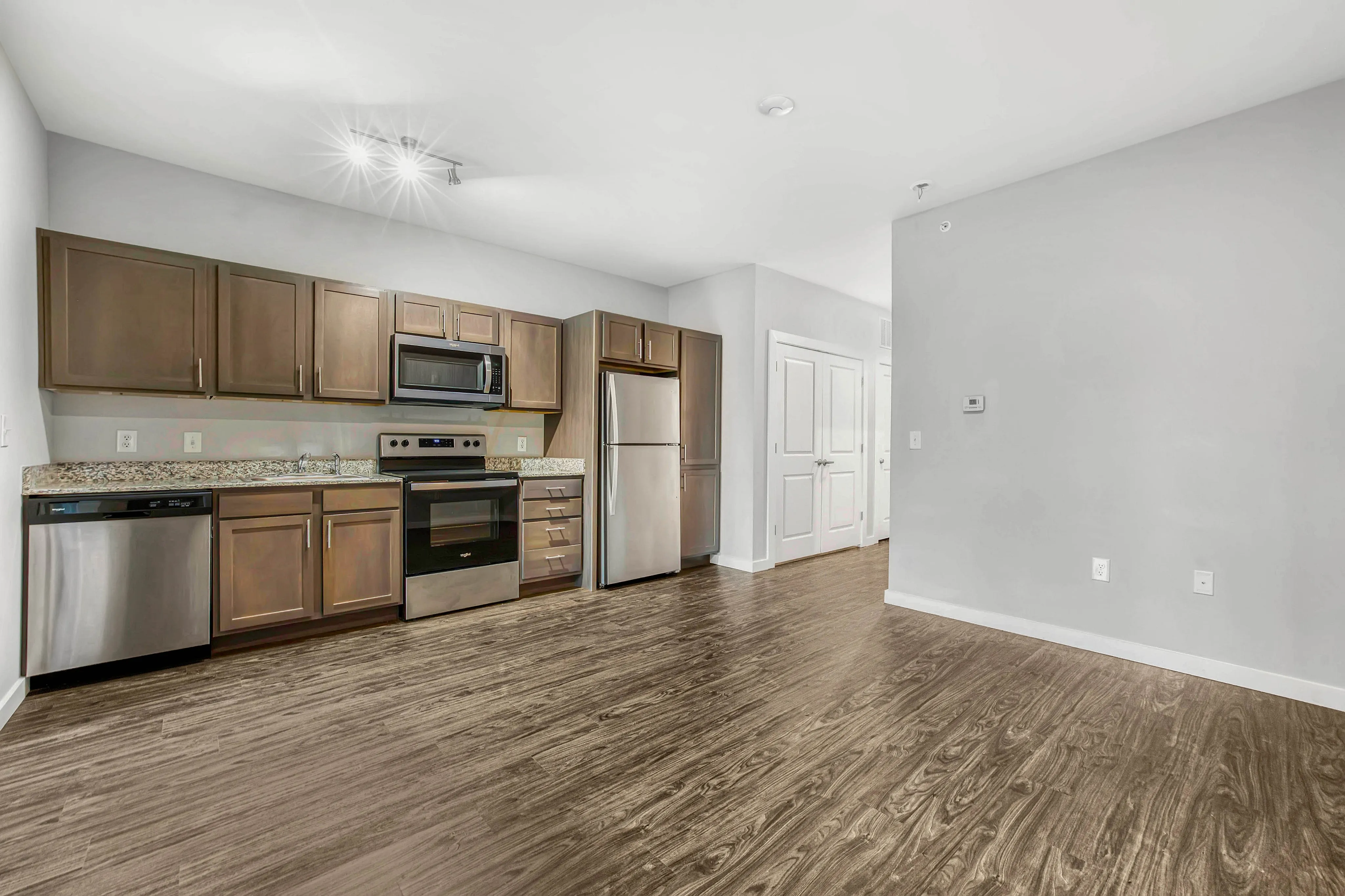 Modern open kitchen with stainless steel appliances, elegant wooden cabinets, and sleek hardwood flooring.