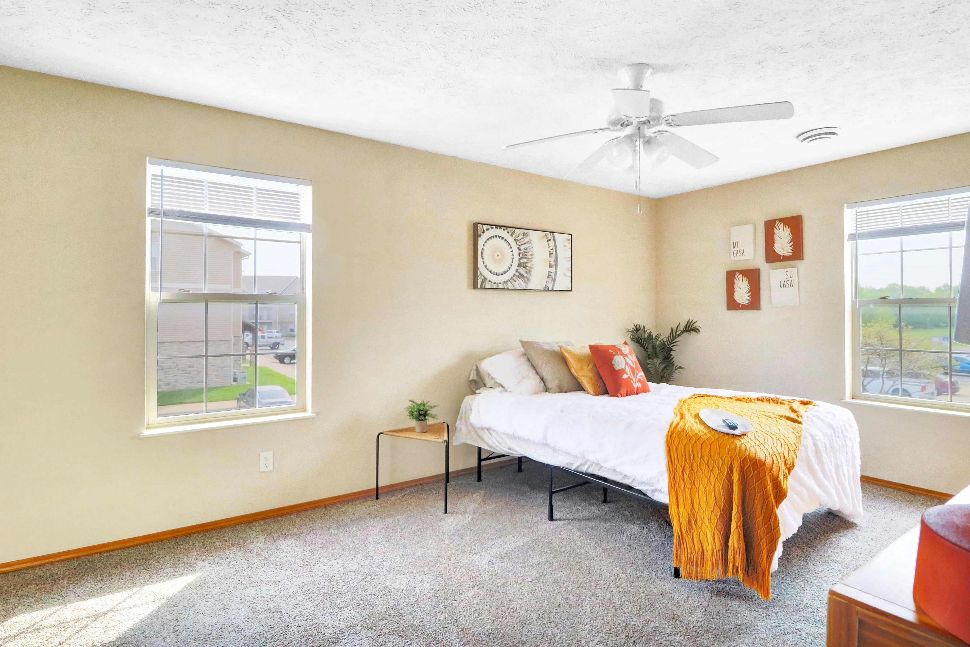Bright and inviting bedroom with elegant decor, featuring large windows, plush carpeting, and a cozy bed adorned with colorful cushions and a stylish throw.