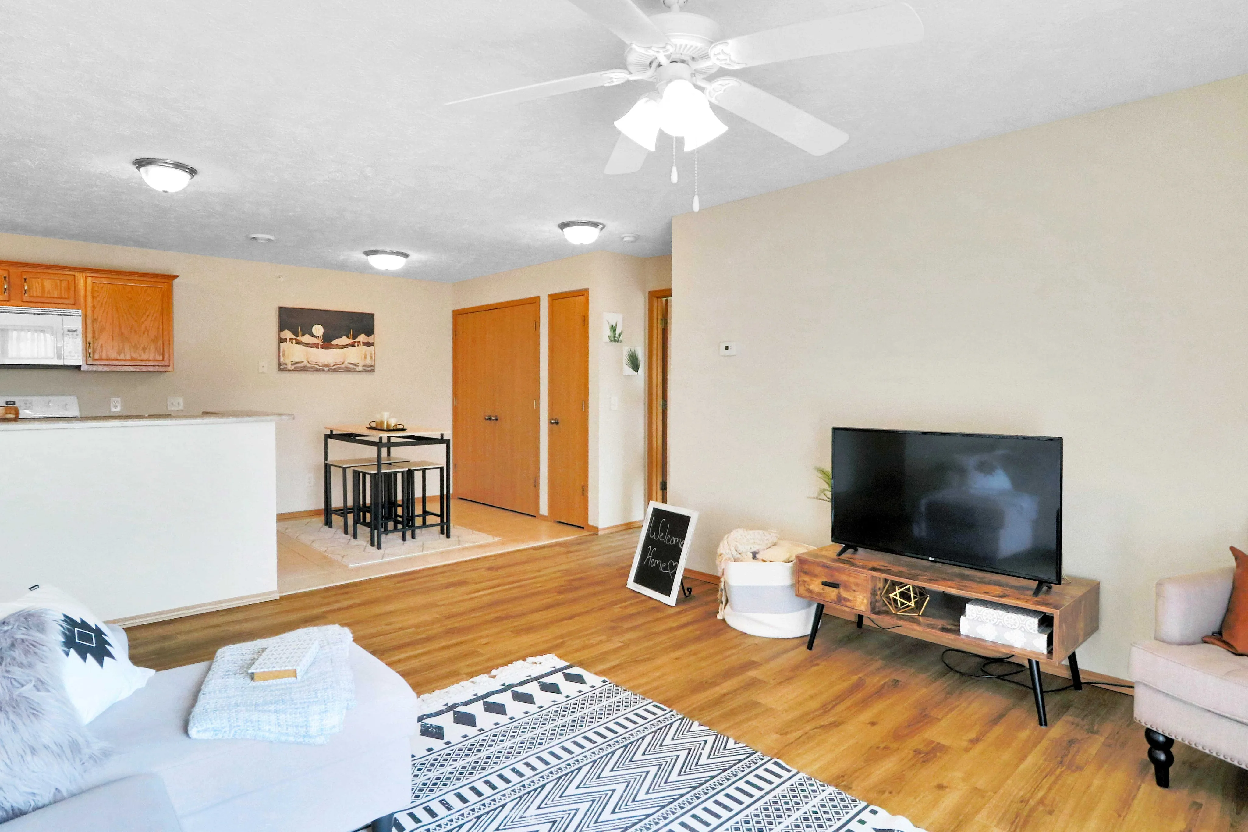 Cozy living area with modern decor, featuring a stylish TV stand, comfortable sofa, and open-plan design leading to a chic dining space and kitchen with warm wooden accents.