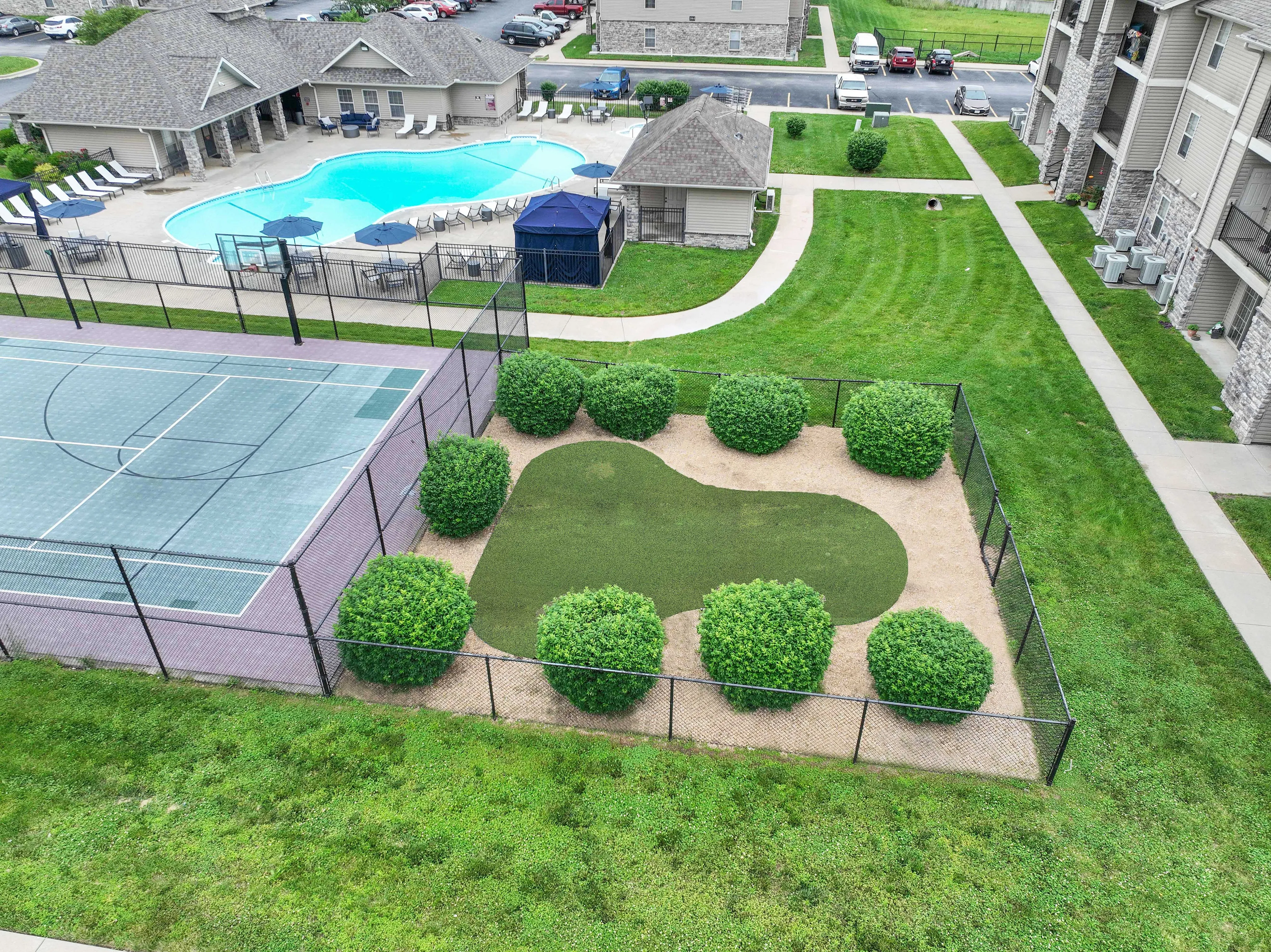 Inviting apartment complex with a sparkling swimming pool, modern tennis court, and lush green landscape, perfect for relaxation and recreation.