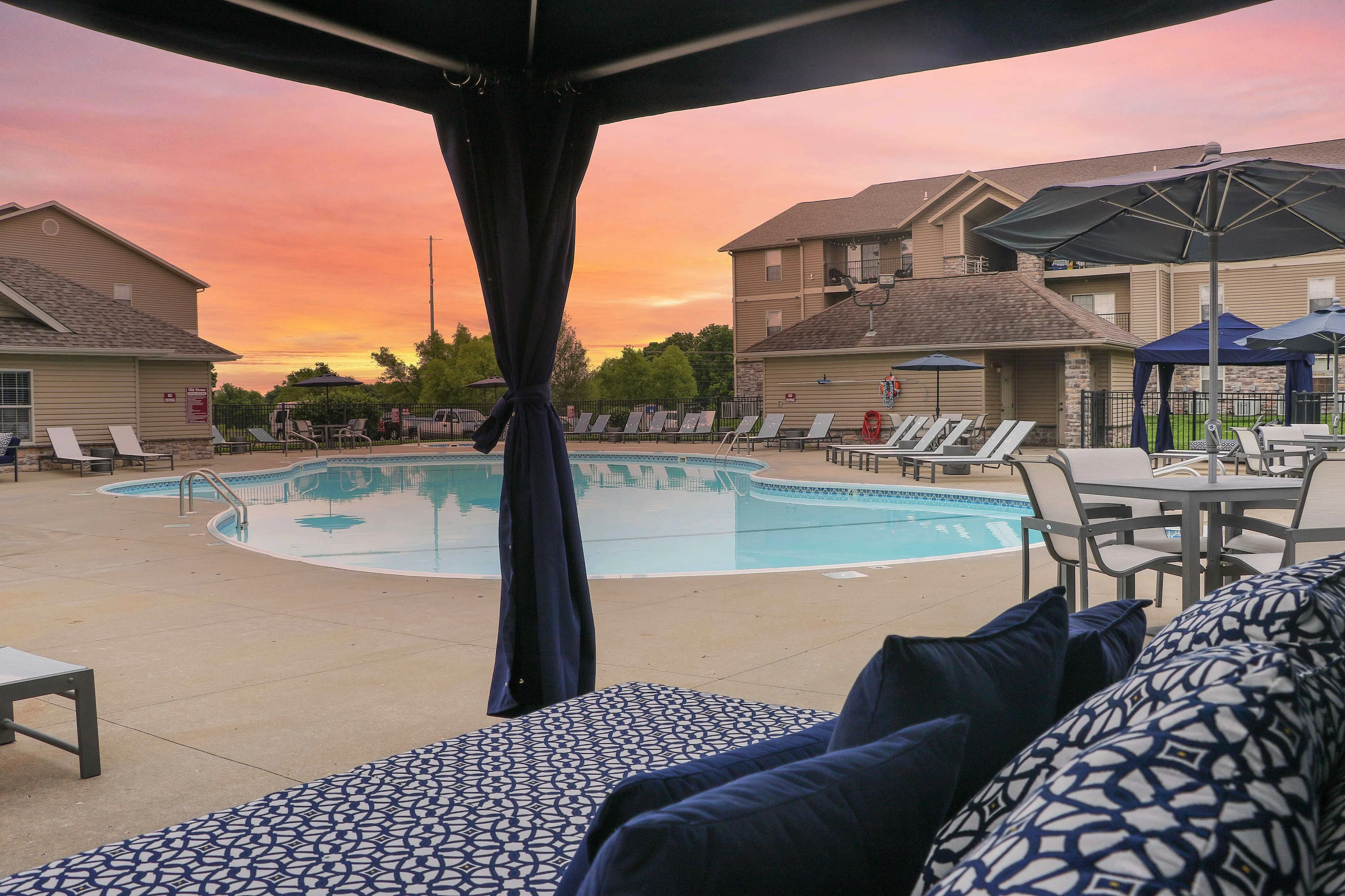 Luxurious poolside retreat with stylish lounge chairs and umbrellas under a vibrant sunset sky.
