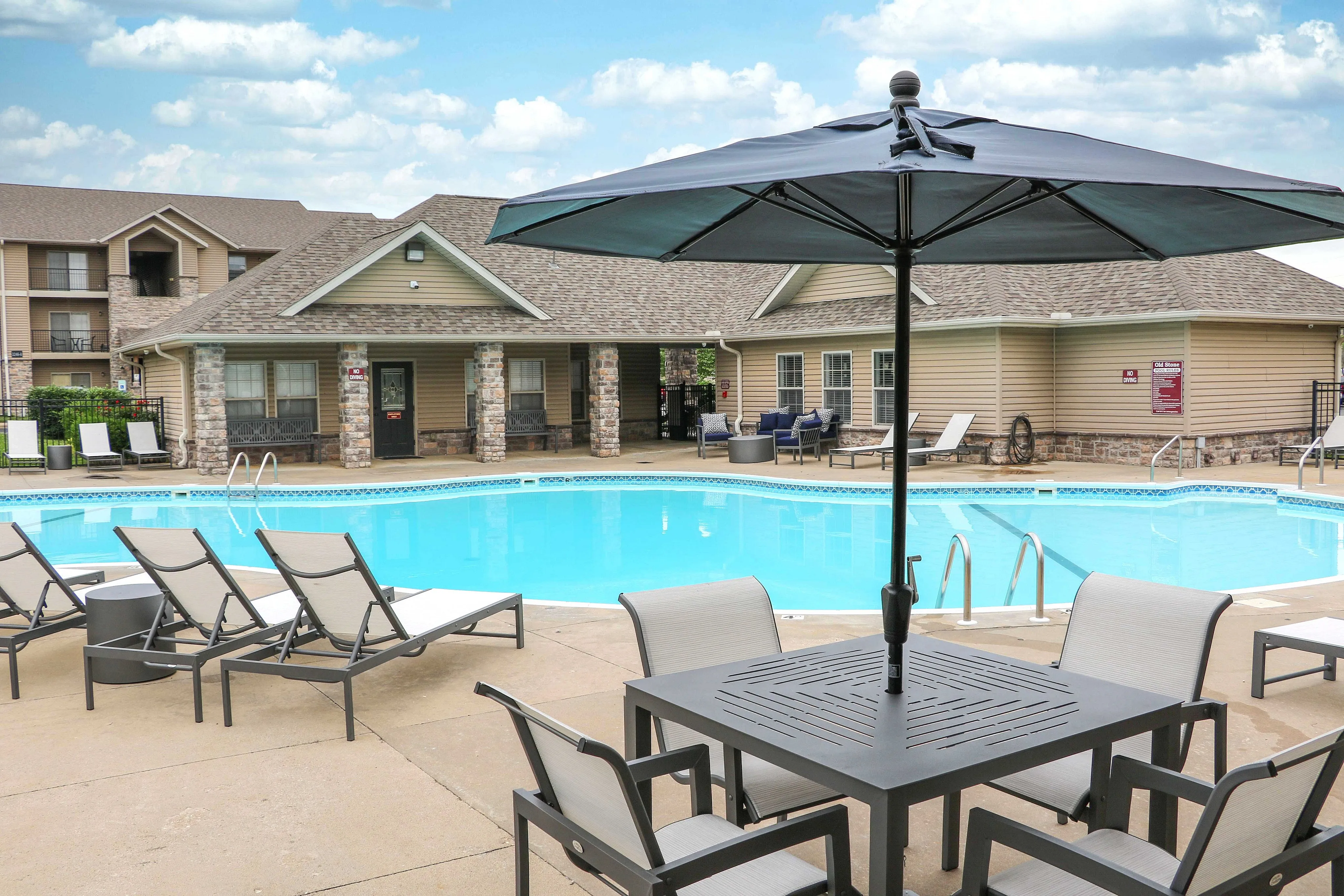 Inviting community pool area featuring relaxing lounge chairs, a stylish umbrella table, and scenic outdoor views, perfect for leisure and enjoyment.