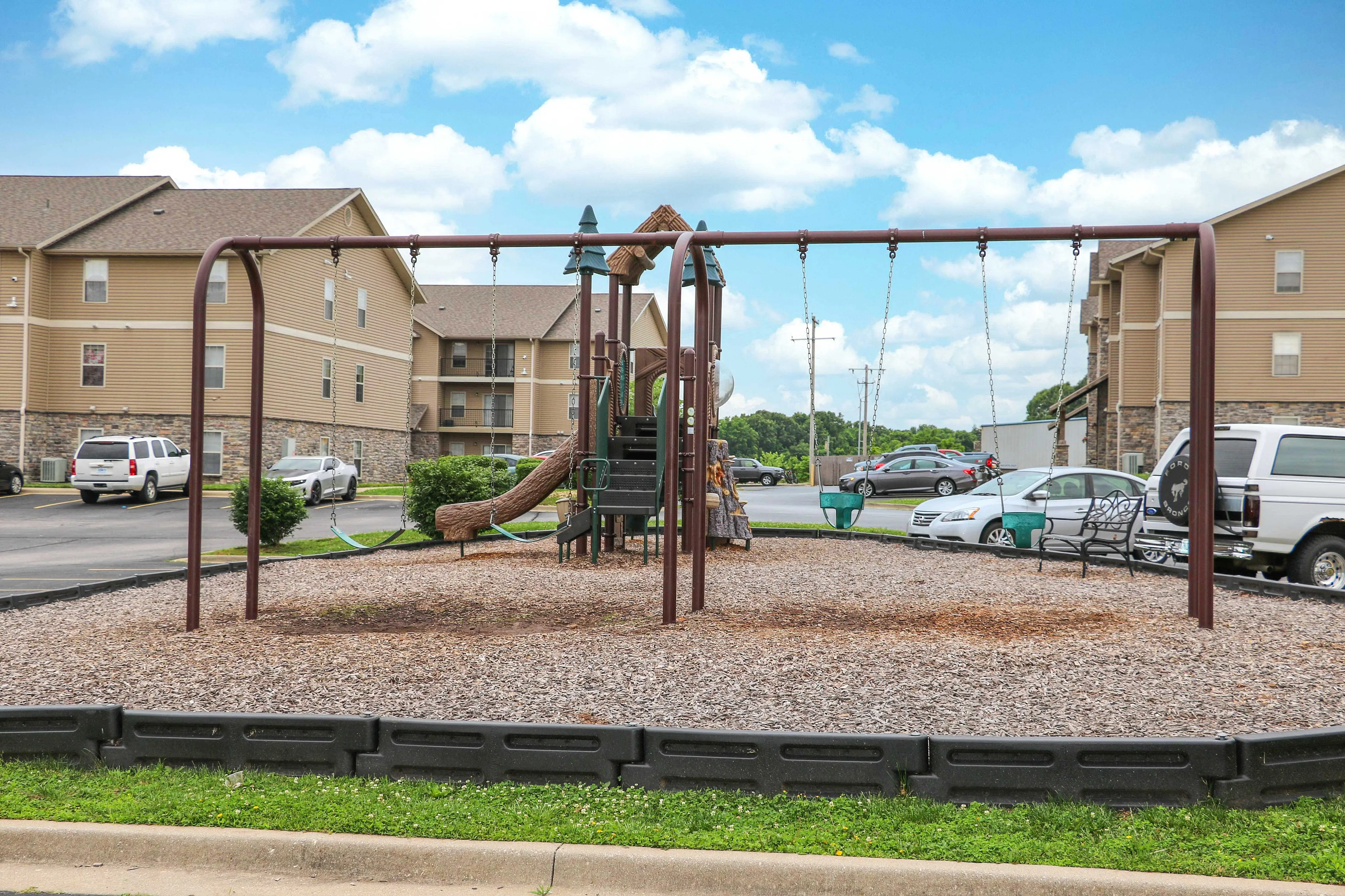 Charming playground area with swings and slide, set against welcoming apartment buildings and lush greenery.