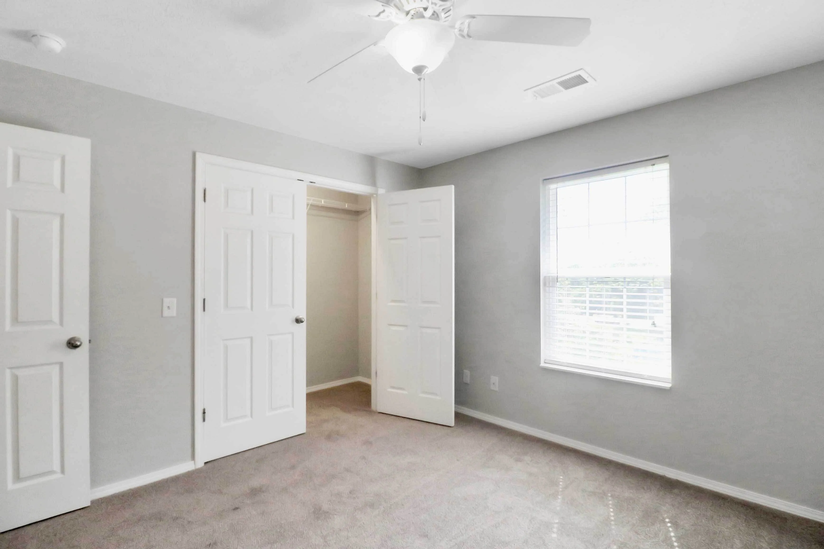 Bright, inviting bedroom featuring soft carpet, natural light from a large window, and a spacious closet with double doors.
