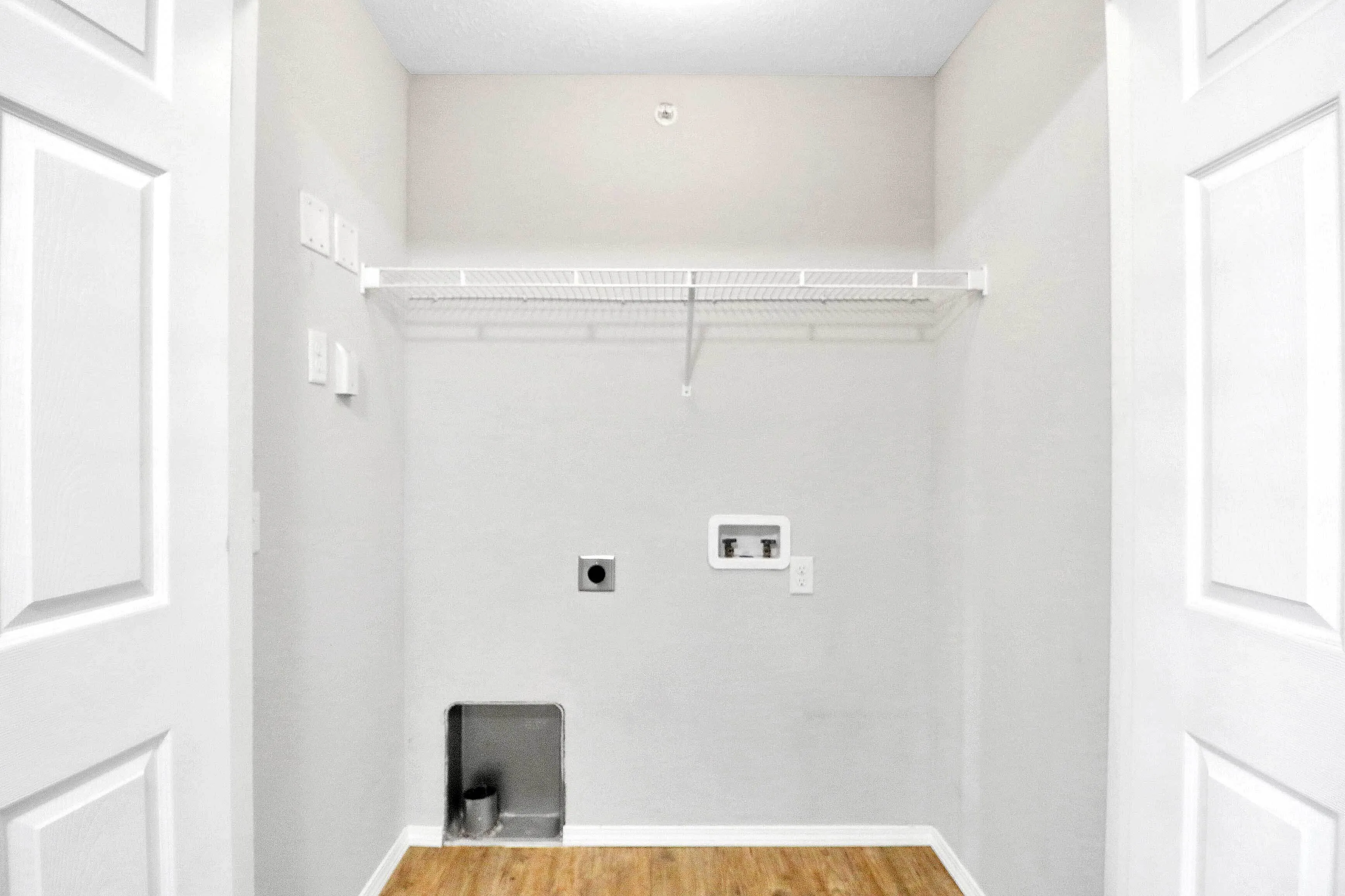 Contemporary laundry room featuring sleek white shelving and modern hookups against a stylish gray wall.