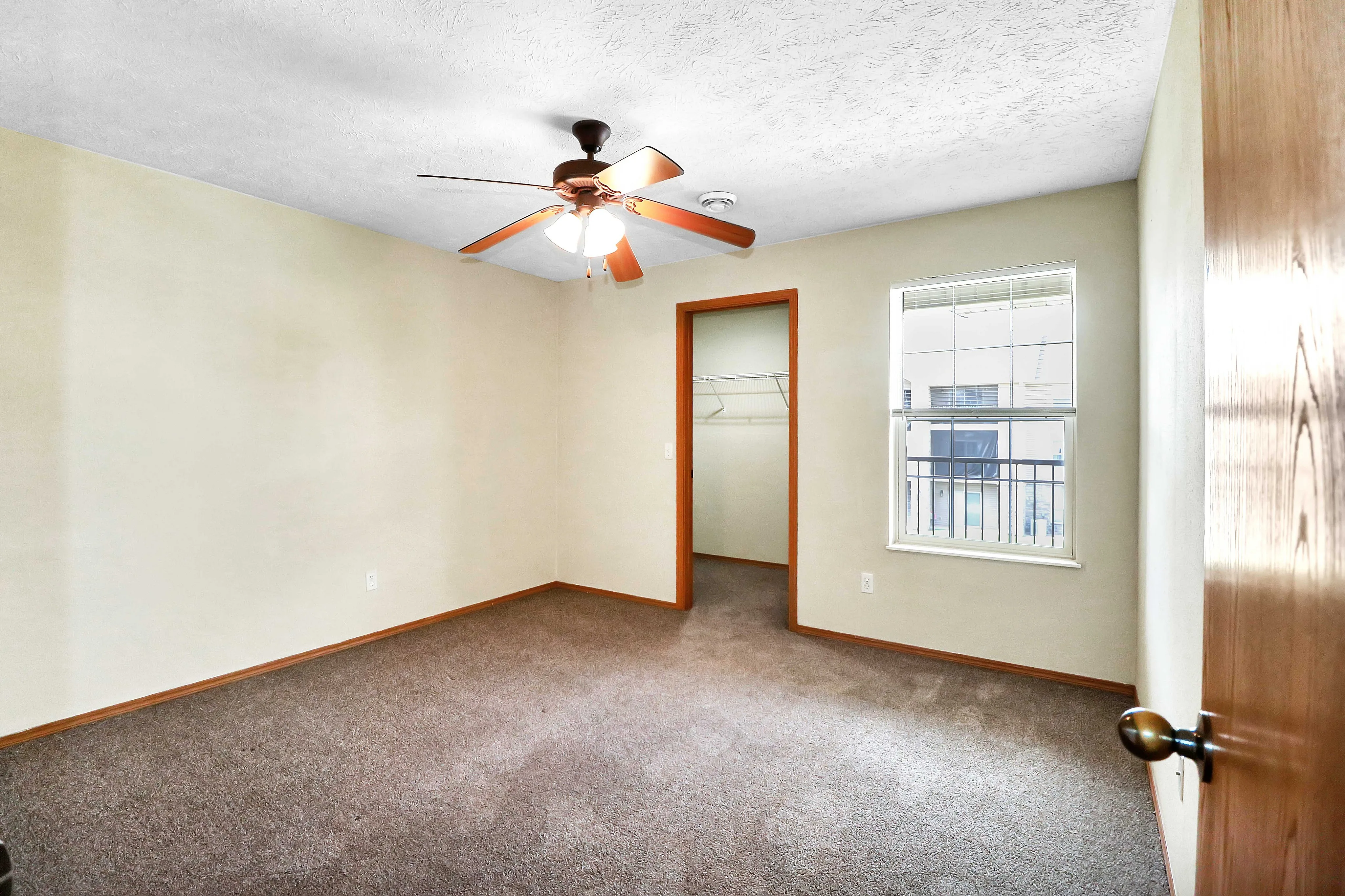 Bright bedroom with cozy carpeting, a ceiling fan, and a spacious walk-in closet, offering comfort and style.