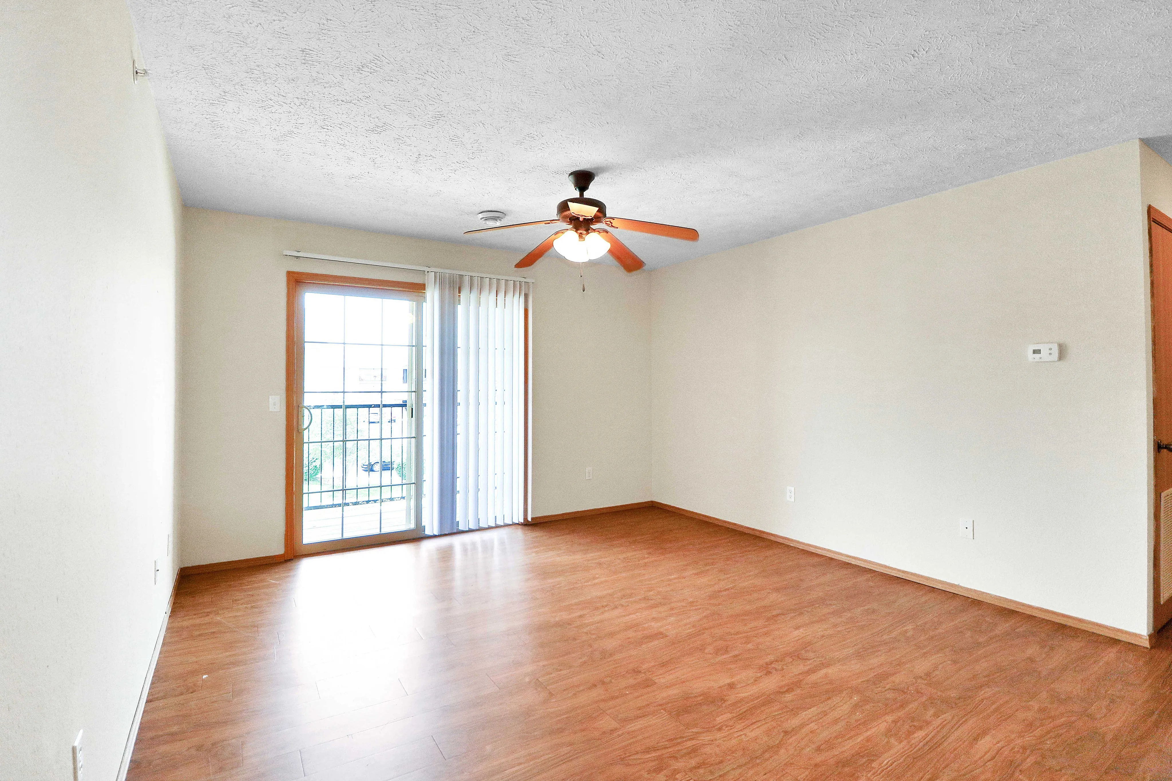 Bright living room with elegant wooden flooring and large sliding glass doors leading to a sunny balcony.