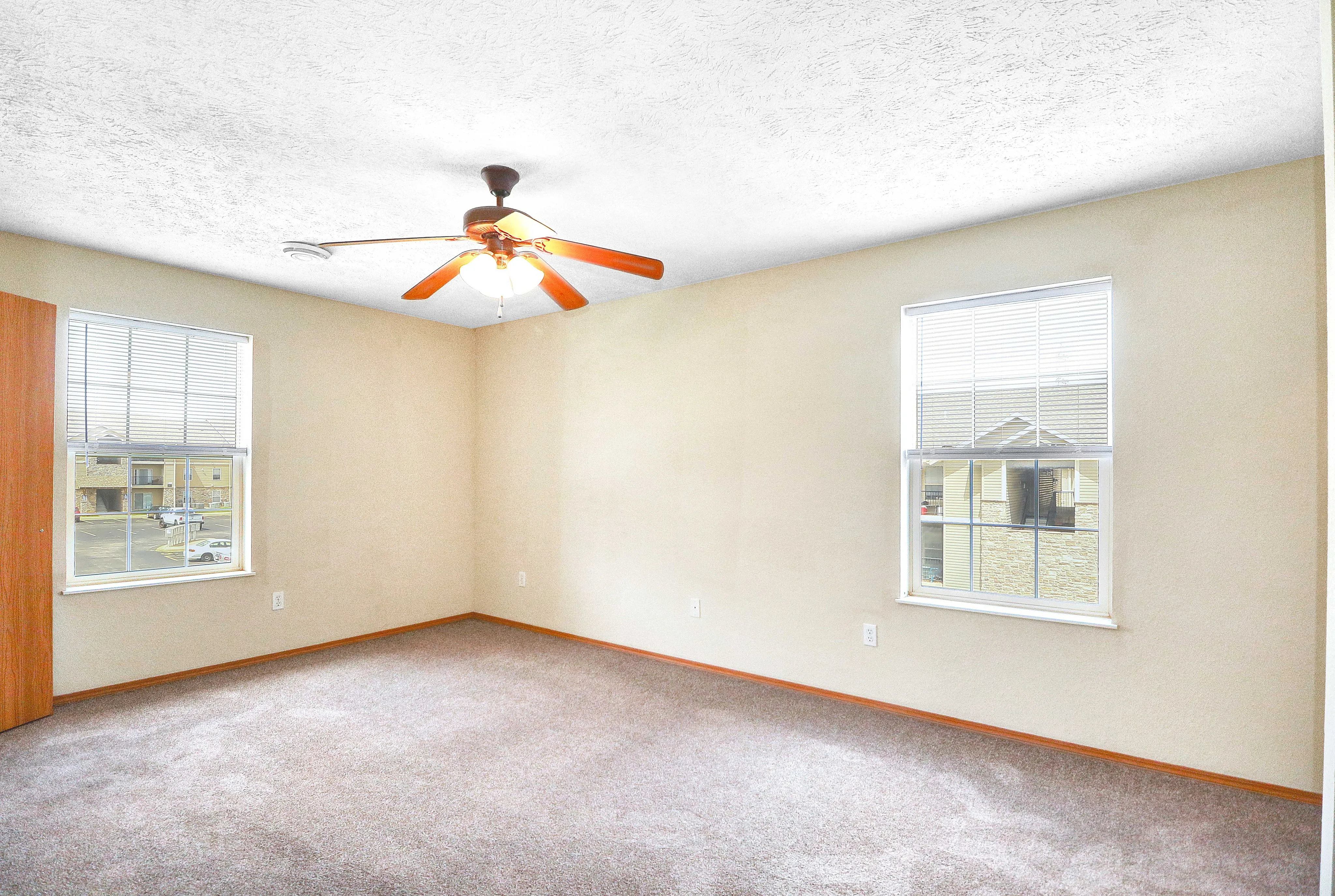 Bright, spacious empty room with large windows and modern ceiling fan, perfect for customization and natural light.
