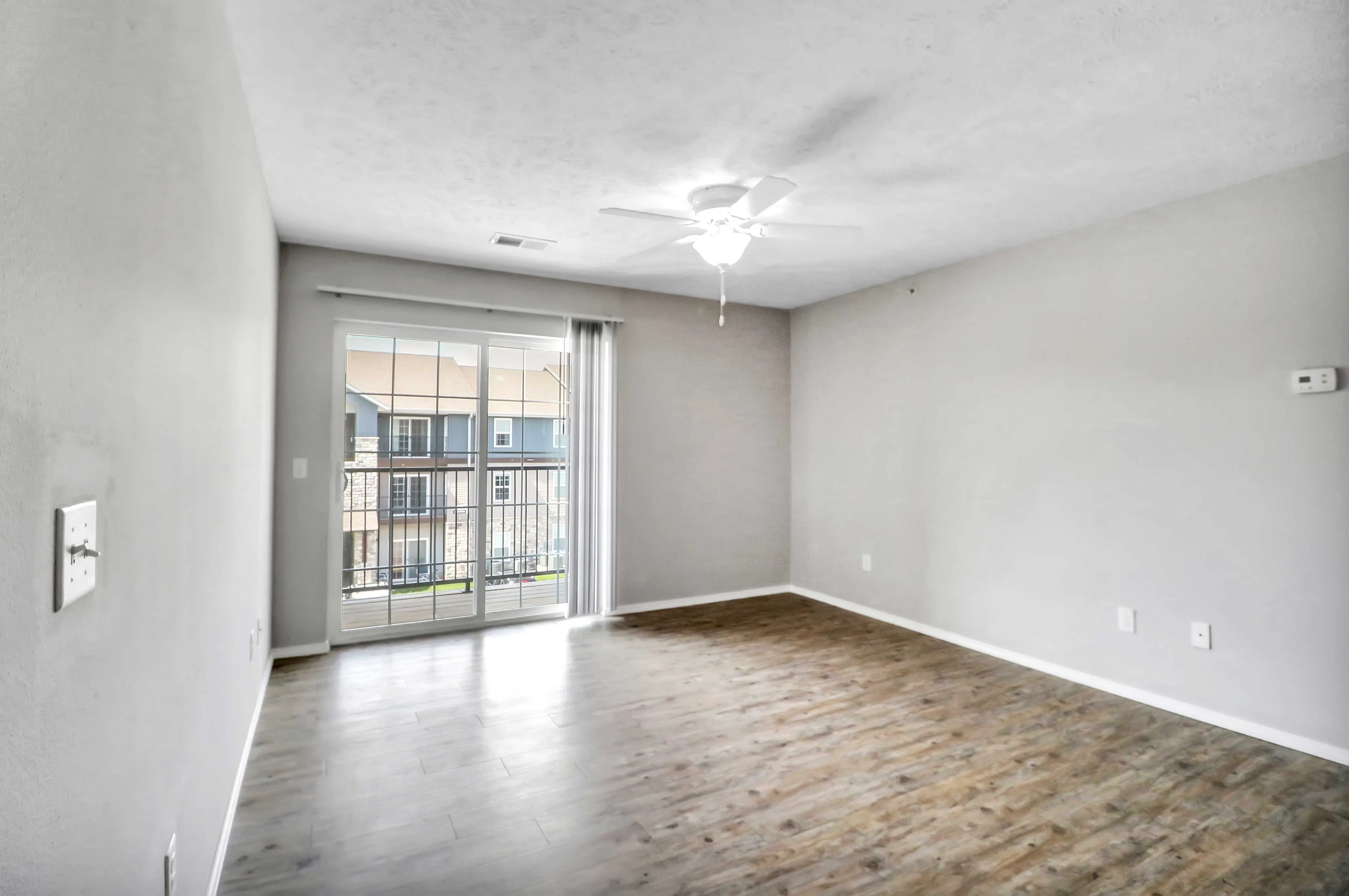Bright and airy living room with elegant wooden flooring, large window doors leading to a scenic balcony view.
