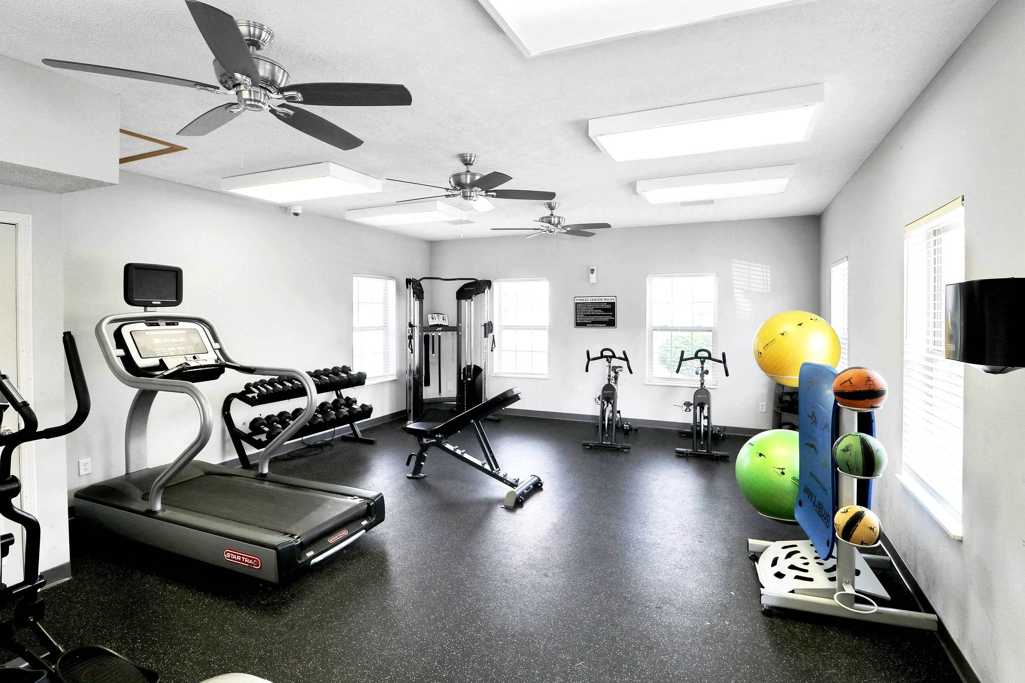 Bright and modern fitness center featuring a treadmill, exercise bikes, weight bench, and vibrant exercise balls, inviting a healthy lifestyle.