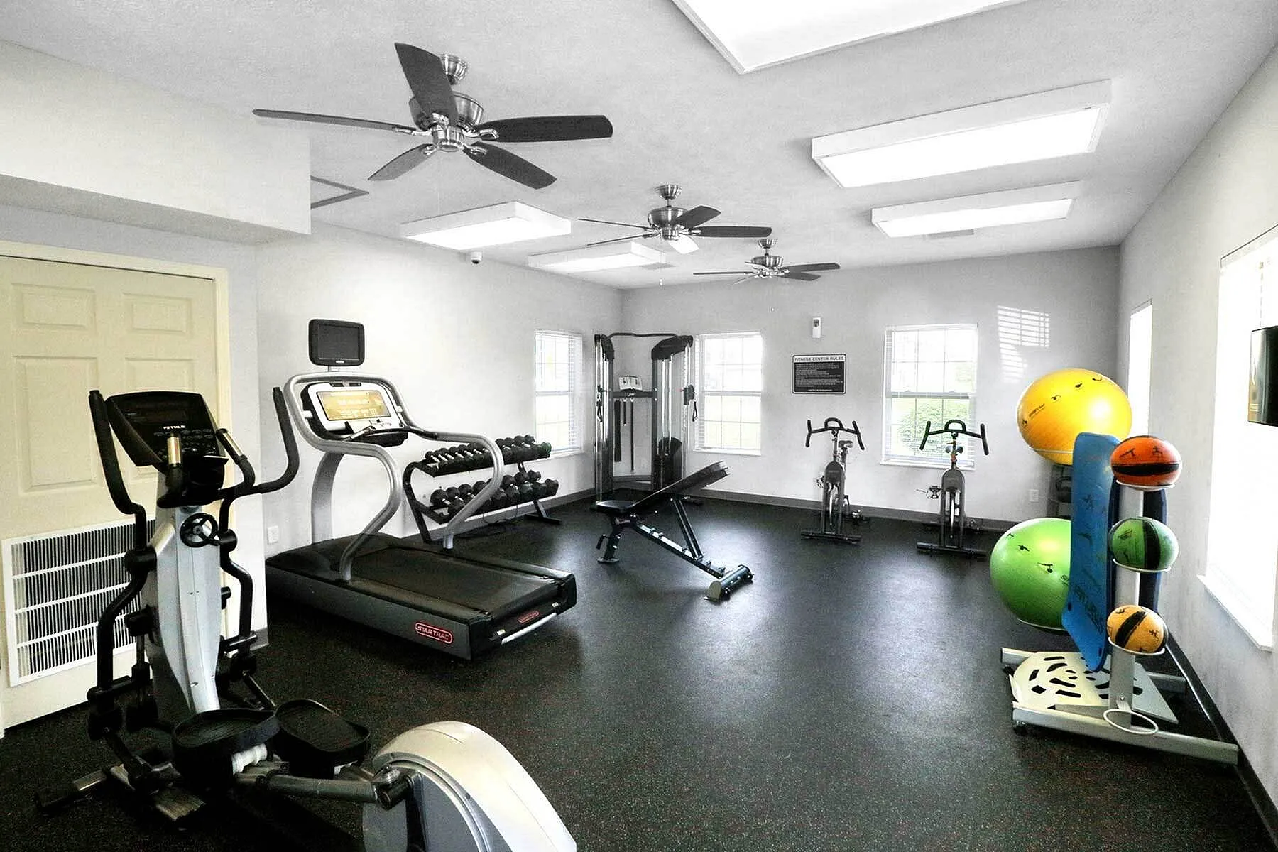 Bright and modern apartment gym featuring state-of-the-art equipment, including treadmills, exercise bikes, and strength training machines, all in a spacious setting with natural light.