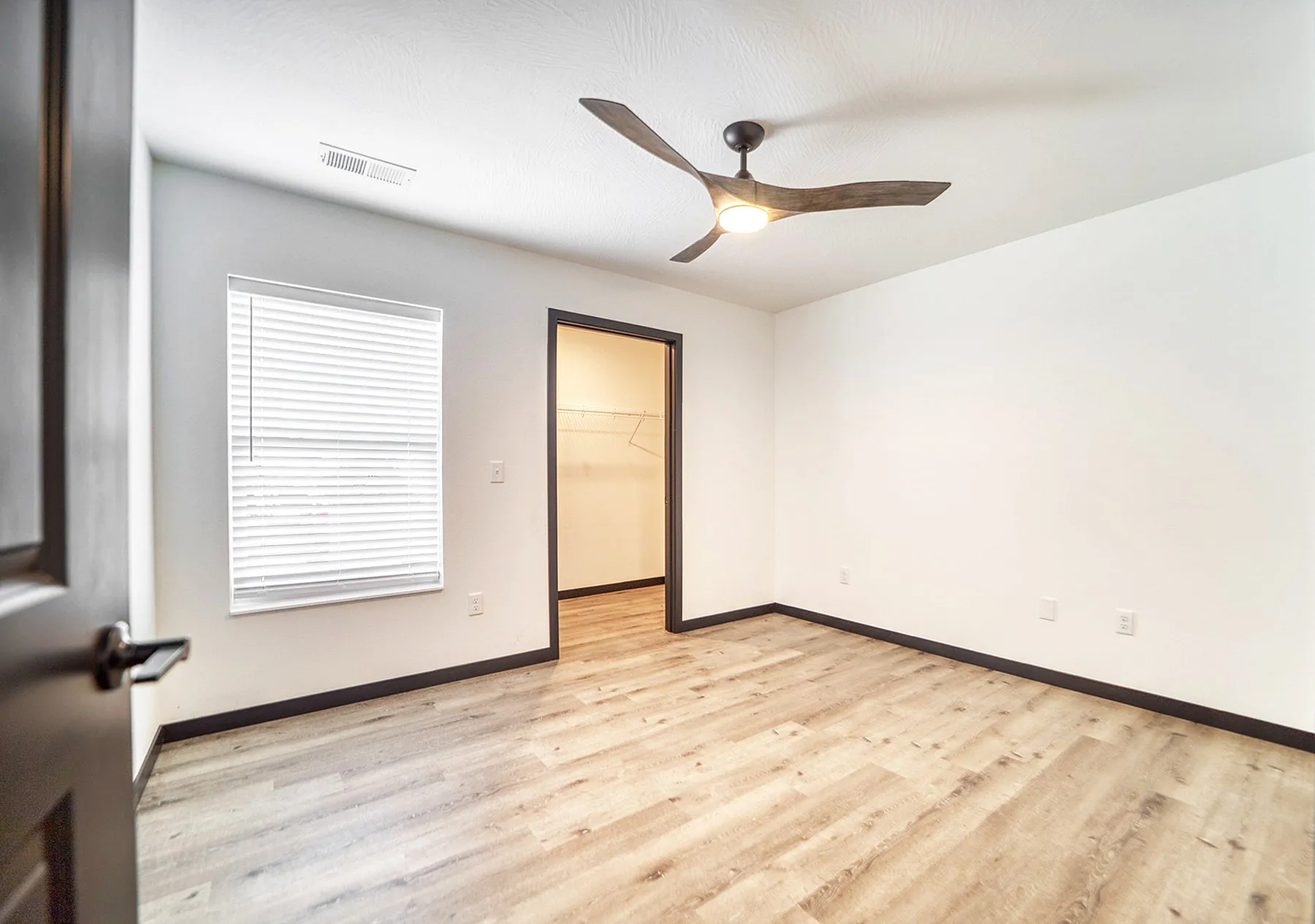 Bright bedroom with sleek wooden flooring, modern ceiling fan, and a walk-in closet.