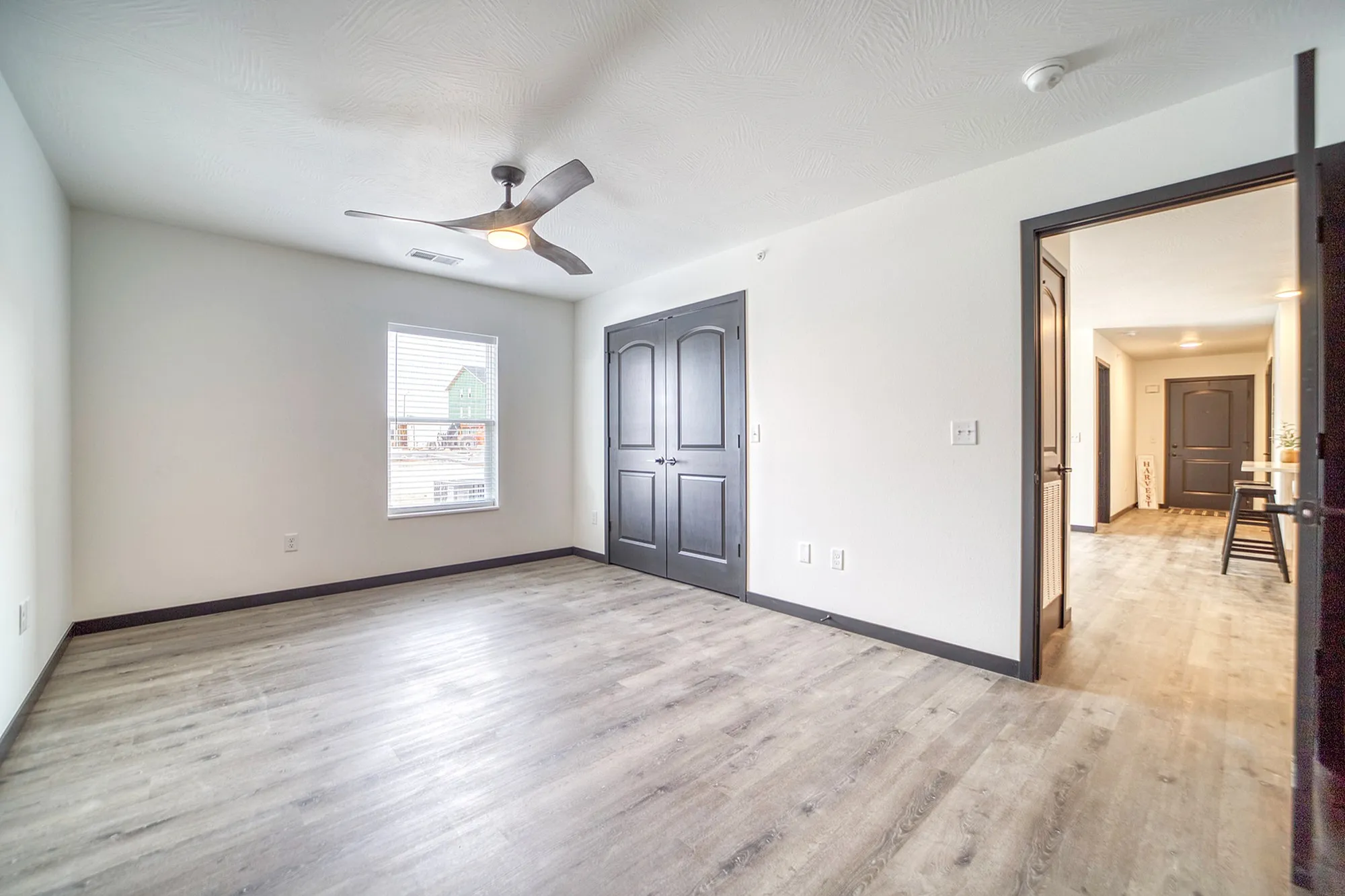Bright and airy room with stylish wood flooring, modern ceiling fan, and elegant dark double doors offering a sleek and inviting ambiance.