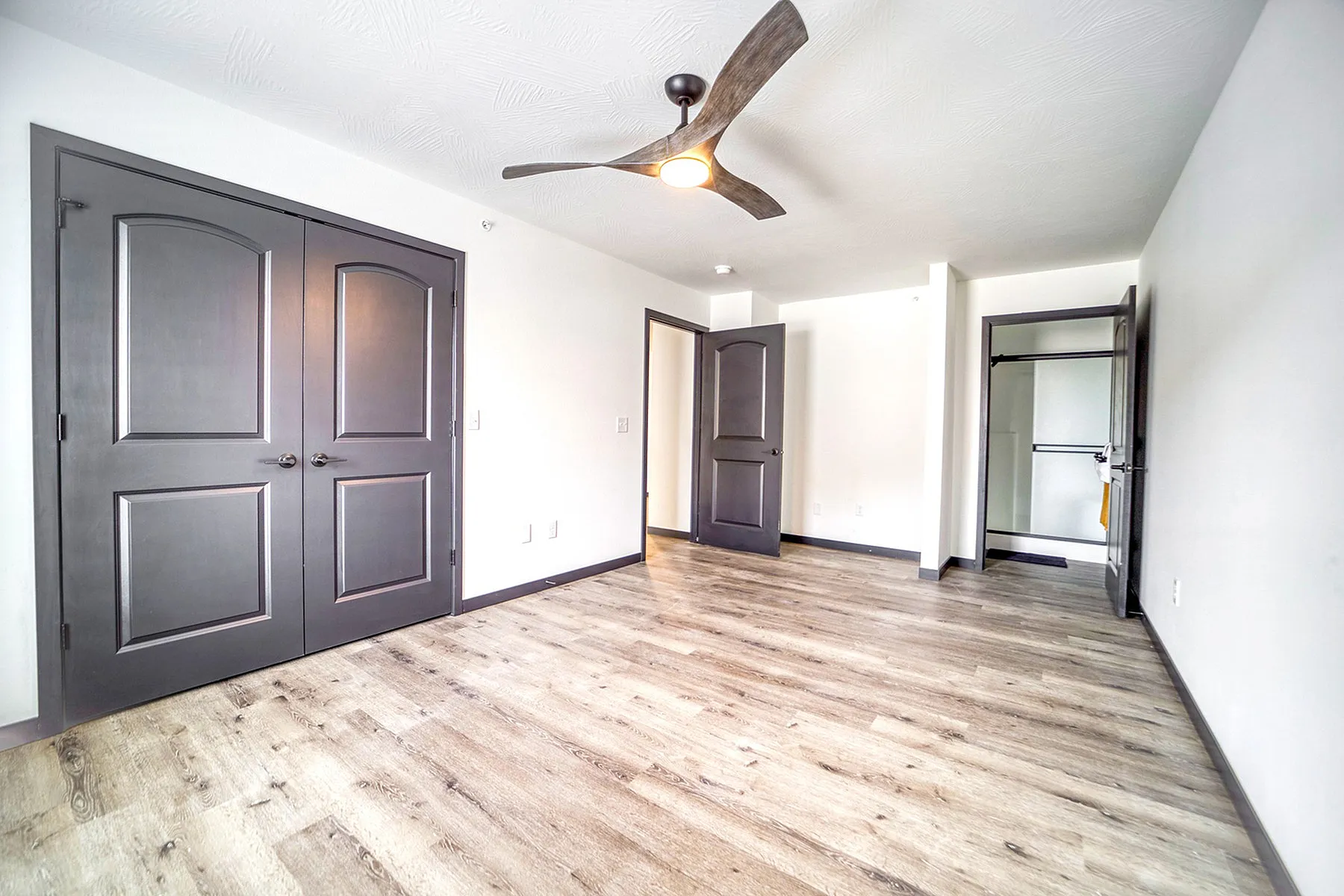 Bright and airy bedroom with elegant double doors, modern ceiling fan, and sleek wooden flooring.