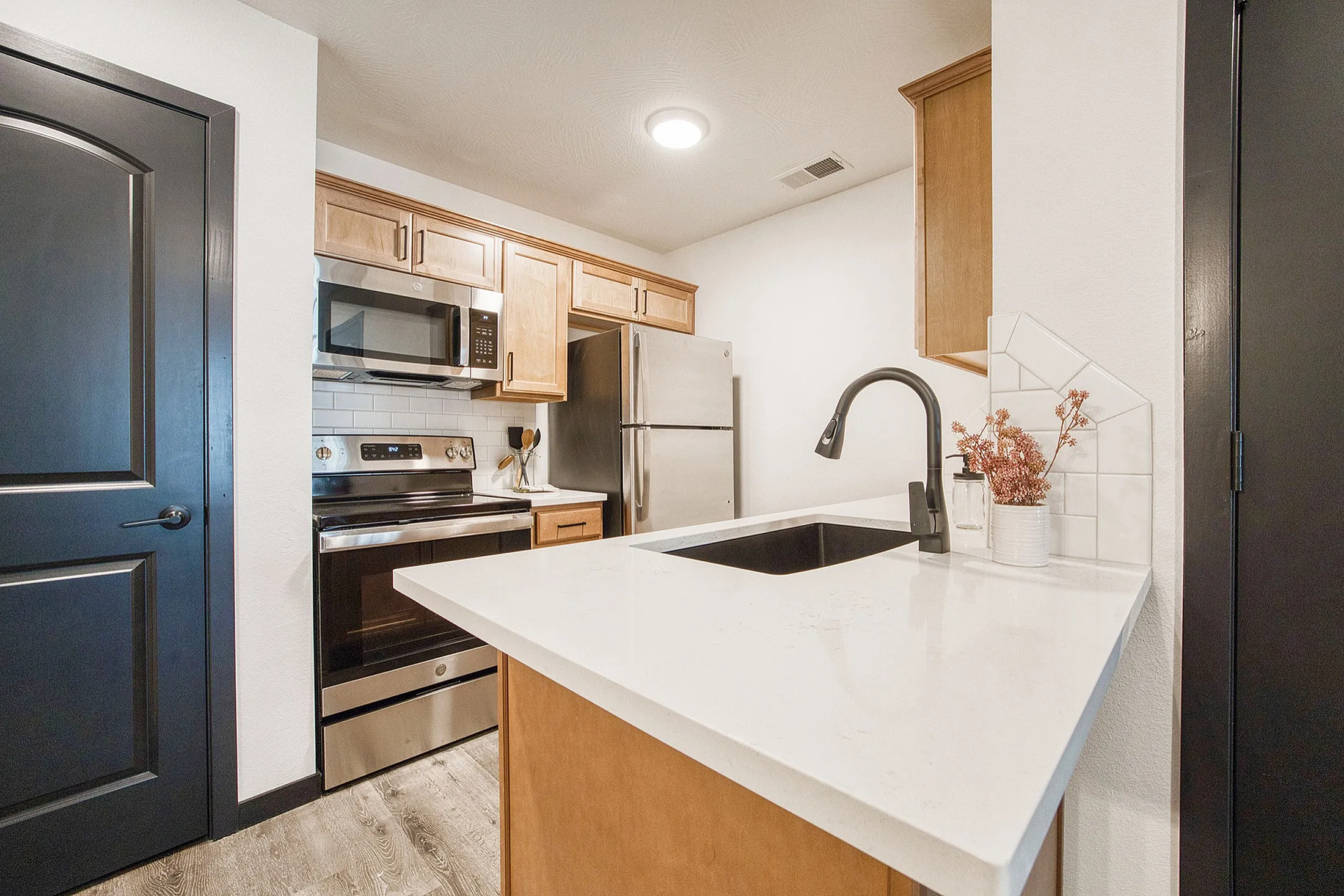 Contemporary kitchen with sleek stainless steel appliances, elegant cabinetry, and a pristine quartz countertop featuring a stylish black faucet.