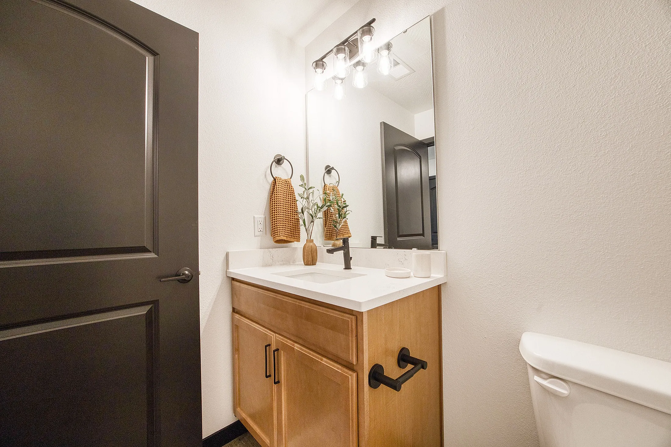 Modern bathroom featuring elegant vanity with a spacious mirror, warm wooden cabinetry, and stylish decor elements.