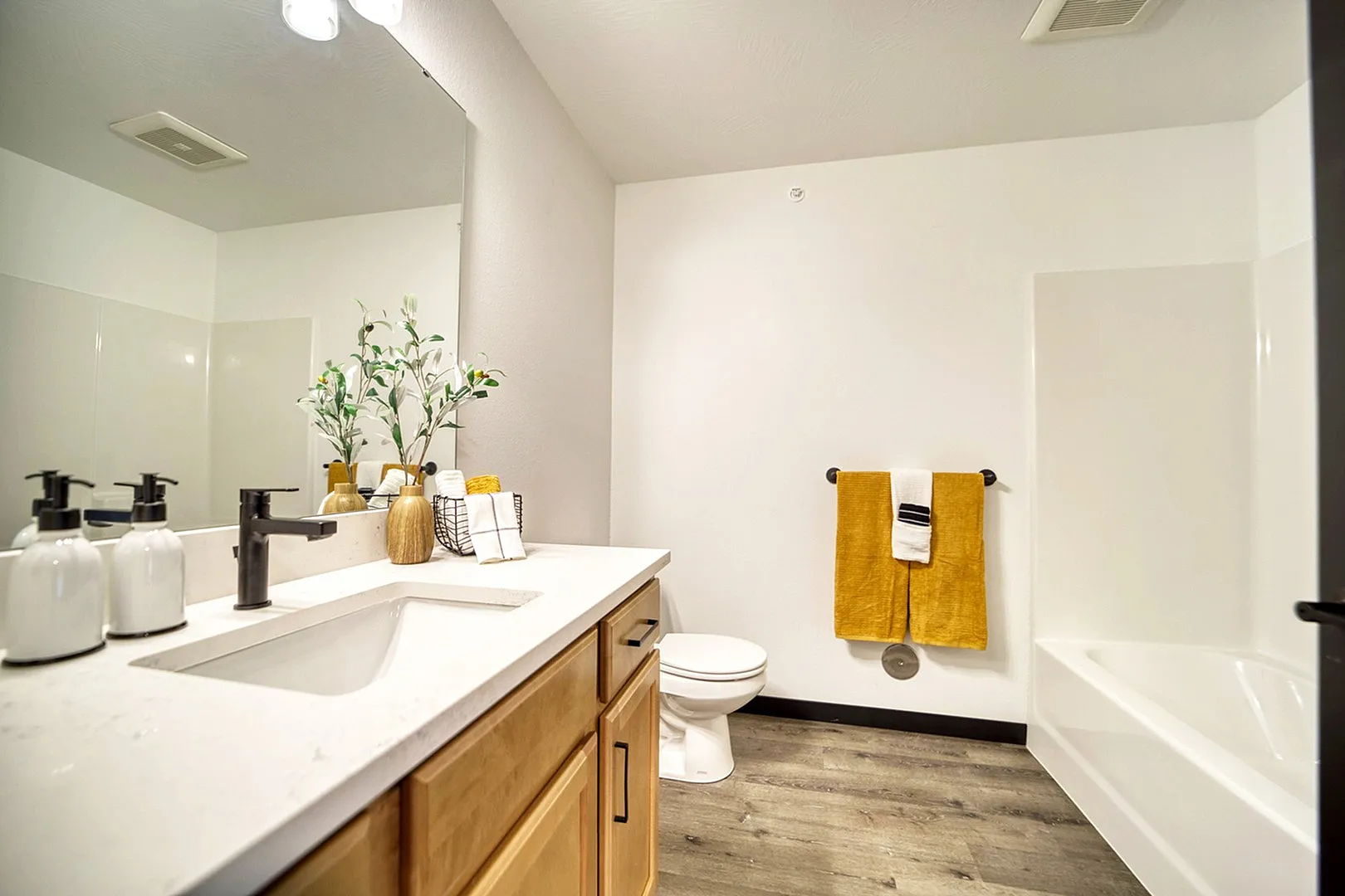 Bright and modern bathroom featuring elegant countertop, stylish faucet, chic accessories, and warm wood flooring.