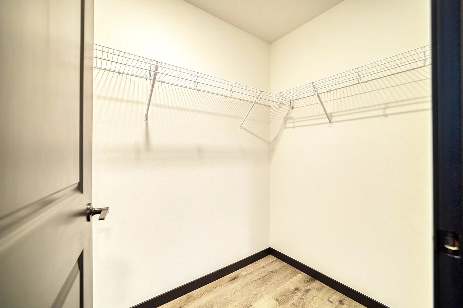 Spacious walk-in closet with sleek wooden flooring and ample shelving space, perfect for organized living.