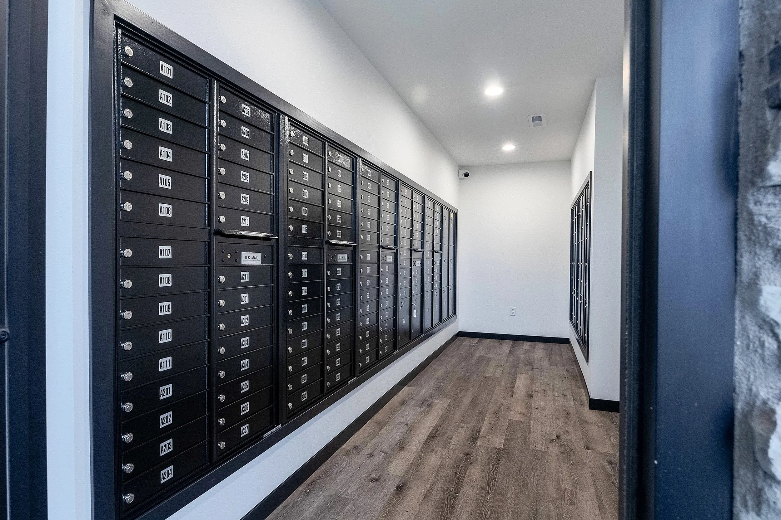 Sleek and modern mailroom with secure, organized mailboxes, featuring elegant wood flooring and bright overhead lighting.