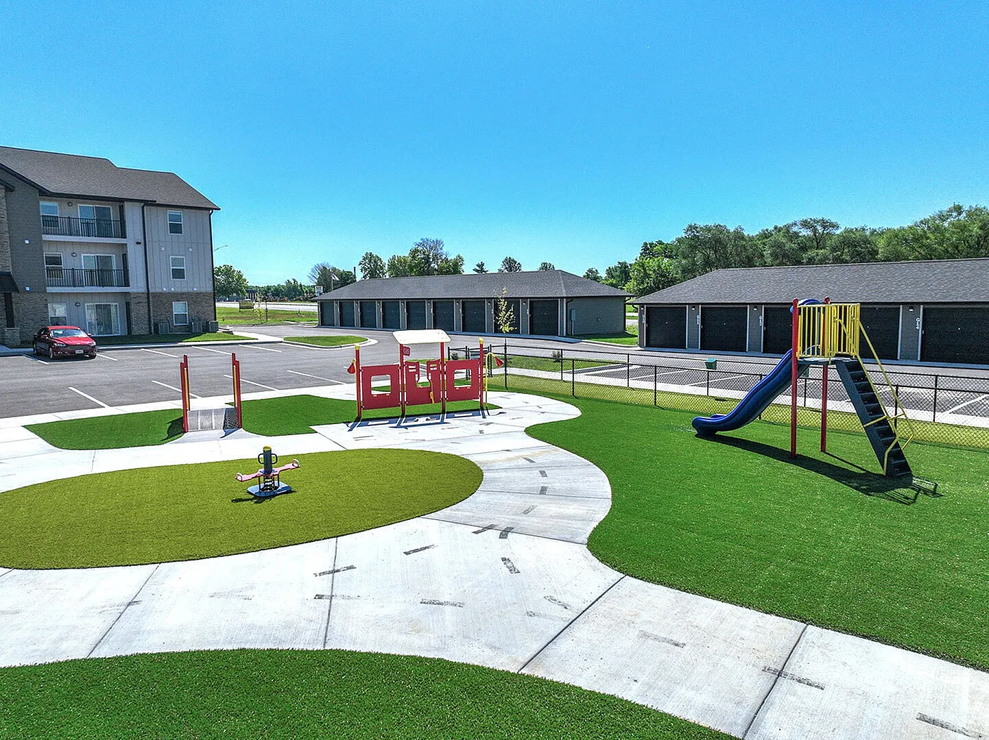 Charming community playground with vibrant green spaces and modern play equipment, surrounded by picturesque apartment buildings under a clear blue sky.