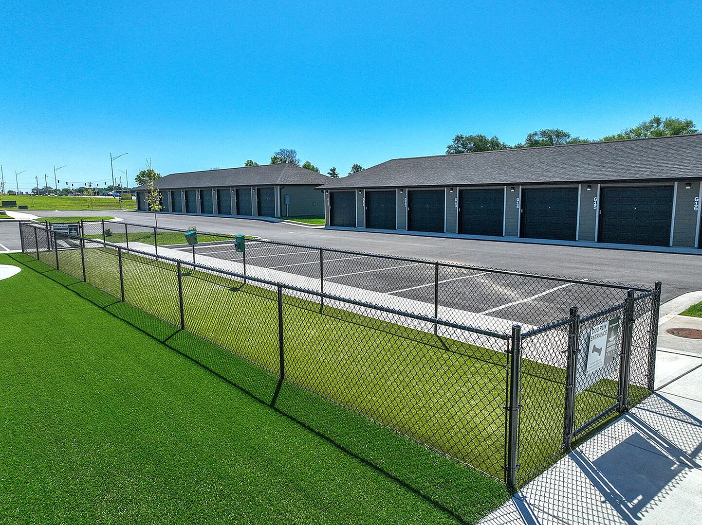 Charming outdoor space featuring a secure fenced pet area with lush green grass, set against modern garages and spacious parking.