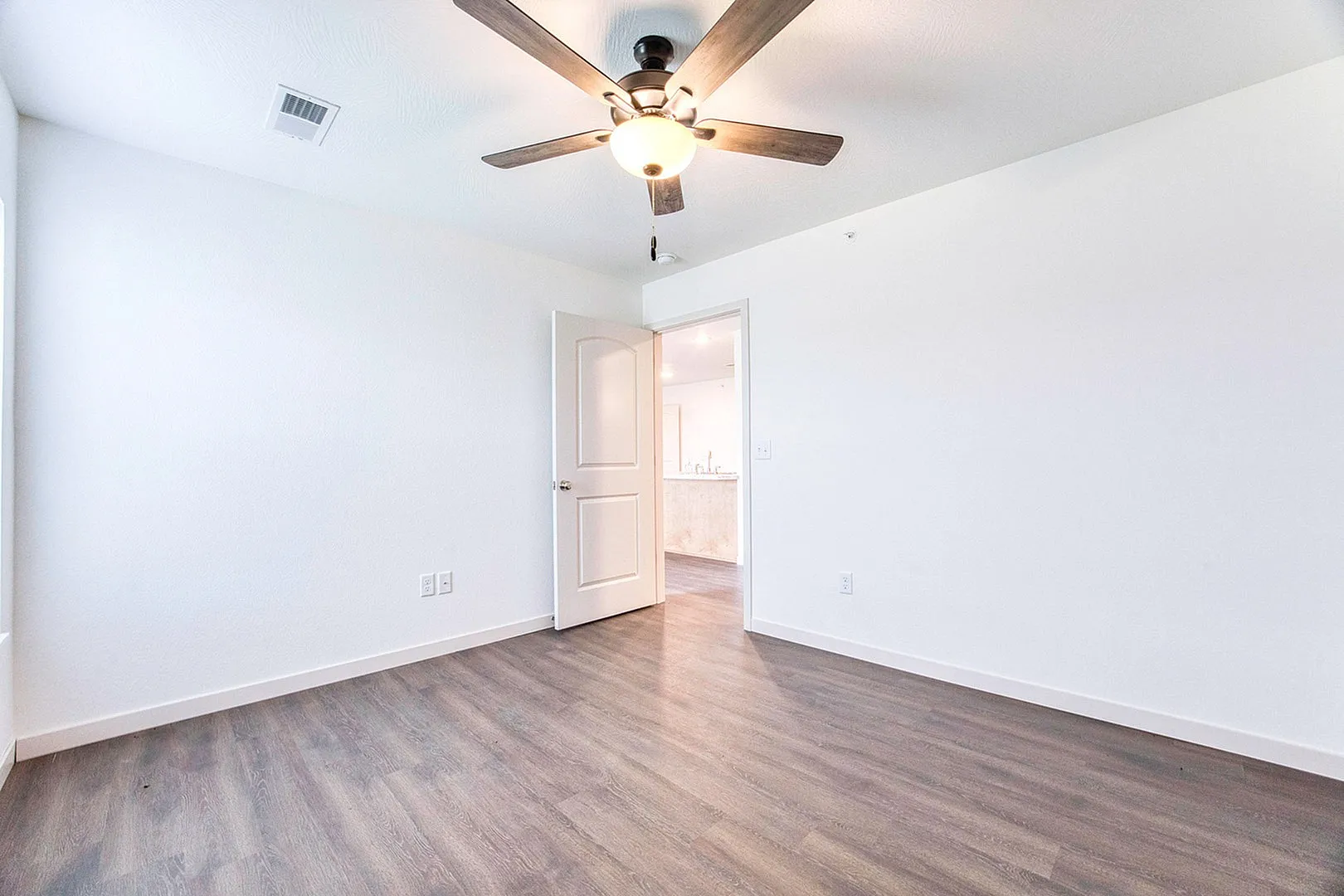 Bright and spacious room featuring sleek hardwood floors and a modern ceiling fan, offering an inviting canvas for personalized design.