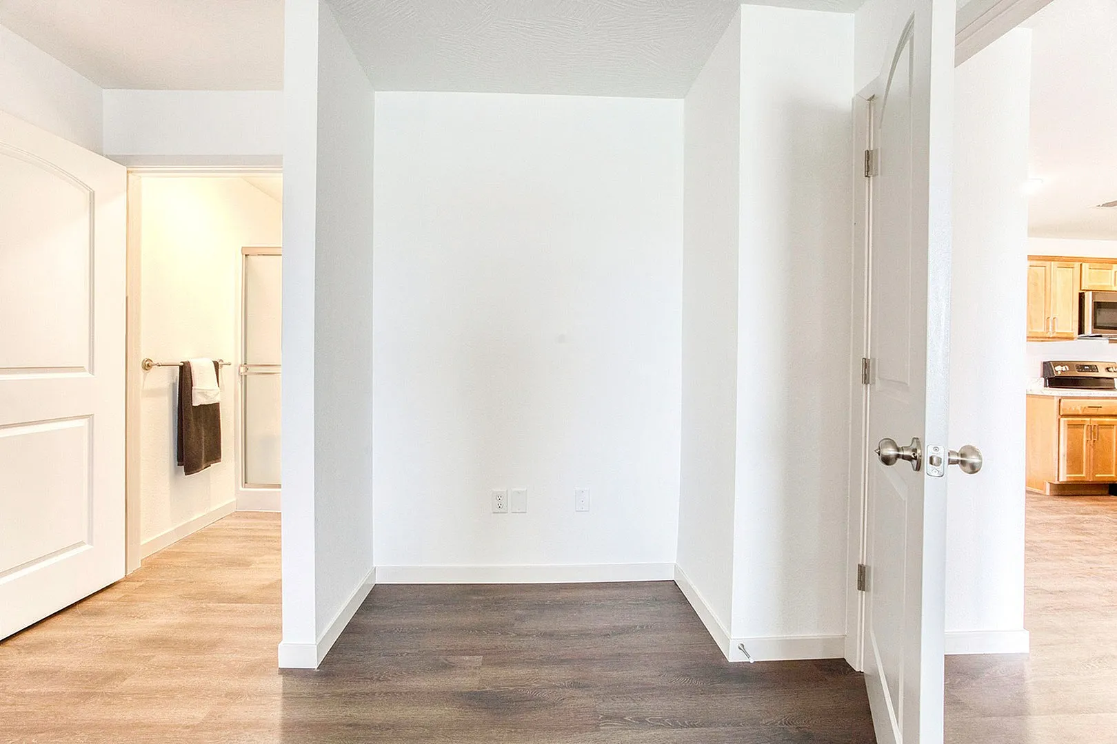 Inviting entryway with elegant wood flooring leading to a modern kitchen and sleek bathroom, perfect for stylish living.