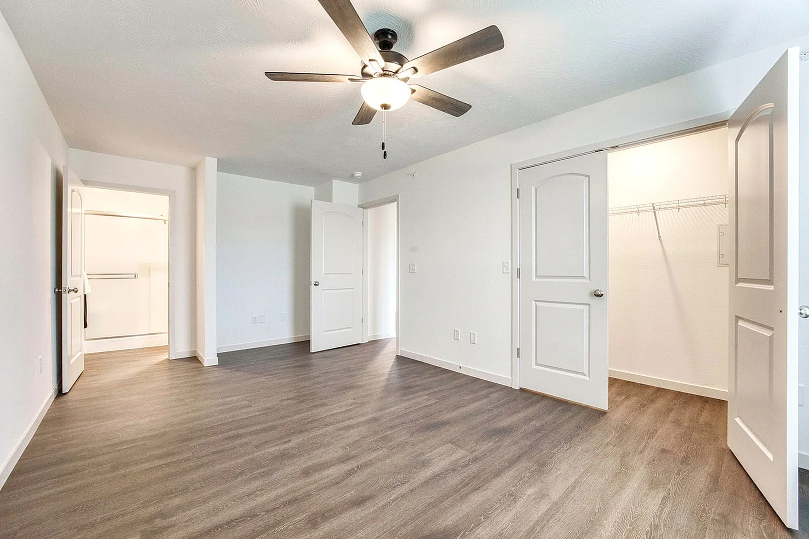 Bright and spacious bedroom with modern hardwood floors, ceiling fan, and generous walk-in closet.