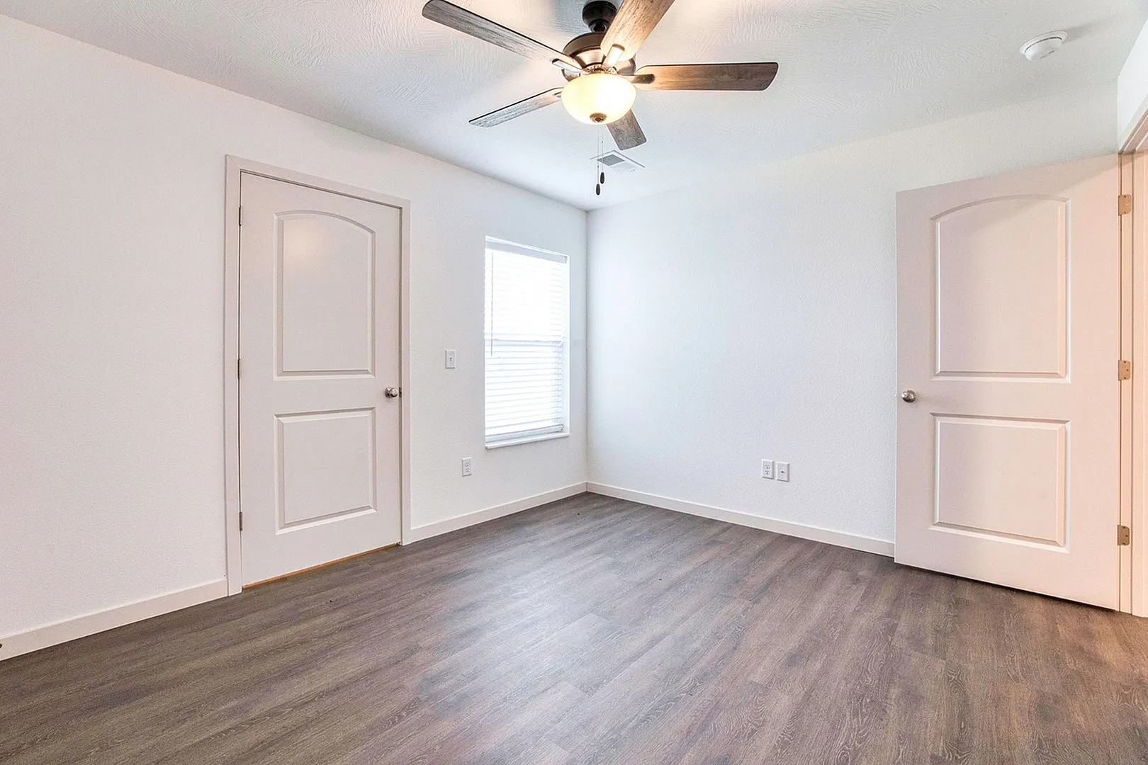Bright room with modern ceiling fan, elegant wood flooring, and crisp white walls, perfect for customization and personalization.