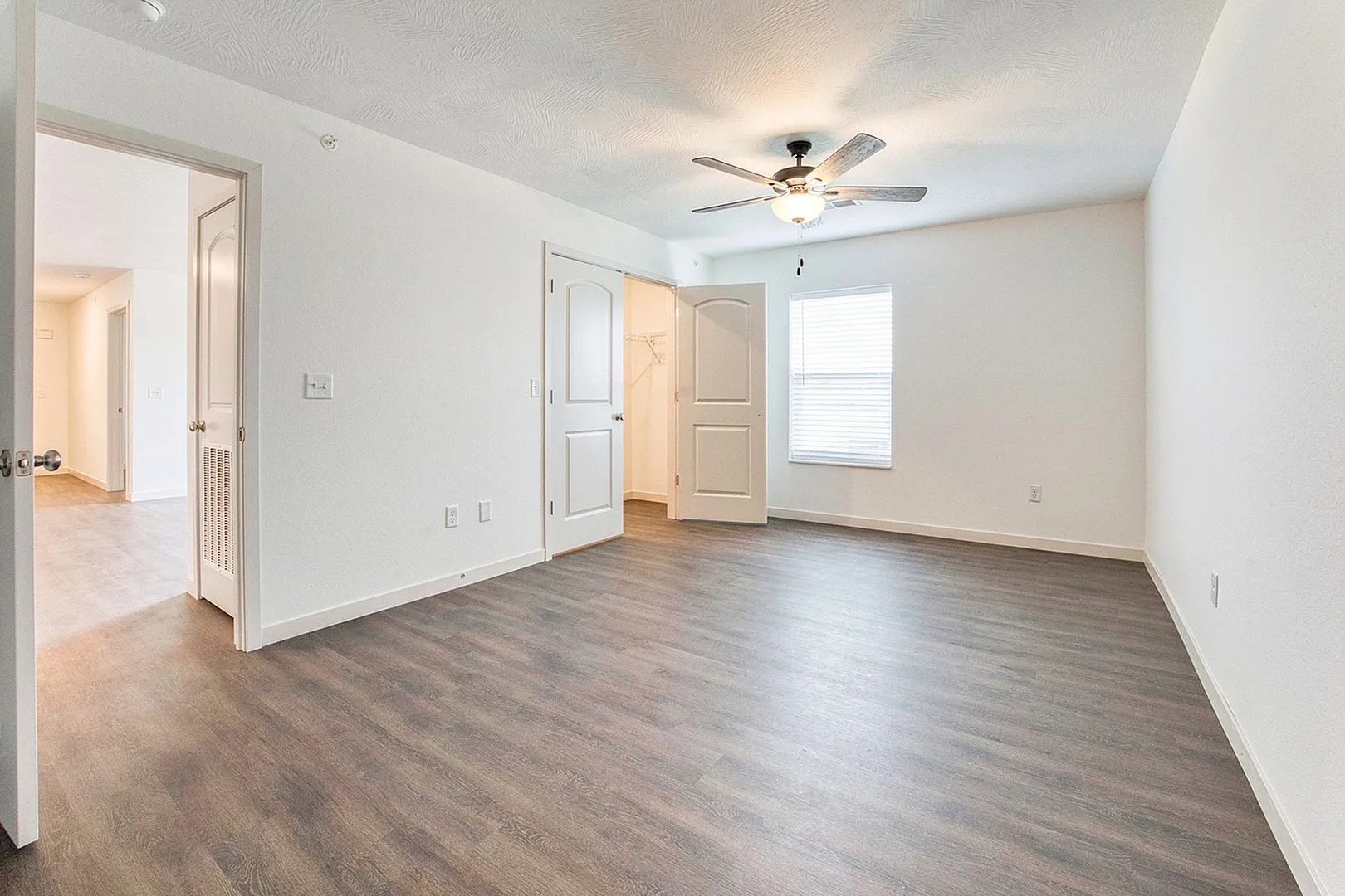 Bright and inviting open bedroom with elegant wood flooring, modern ceiling fan, and a walk-in closet, perfect for comfortable living.