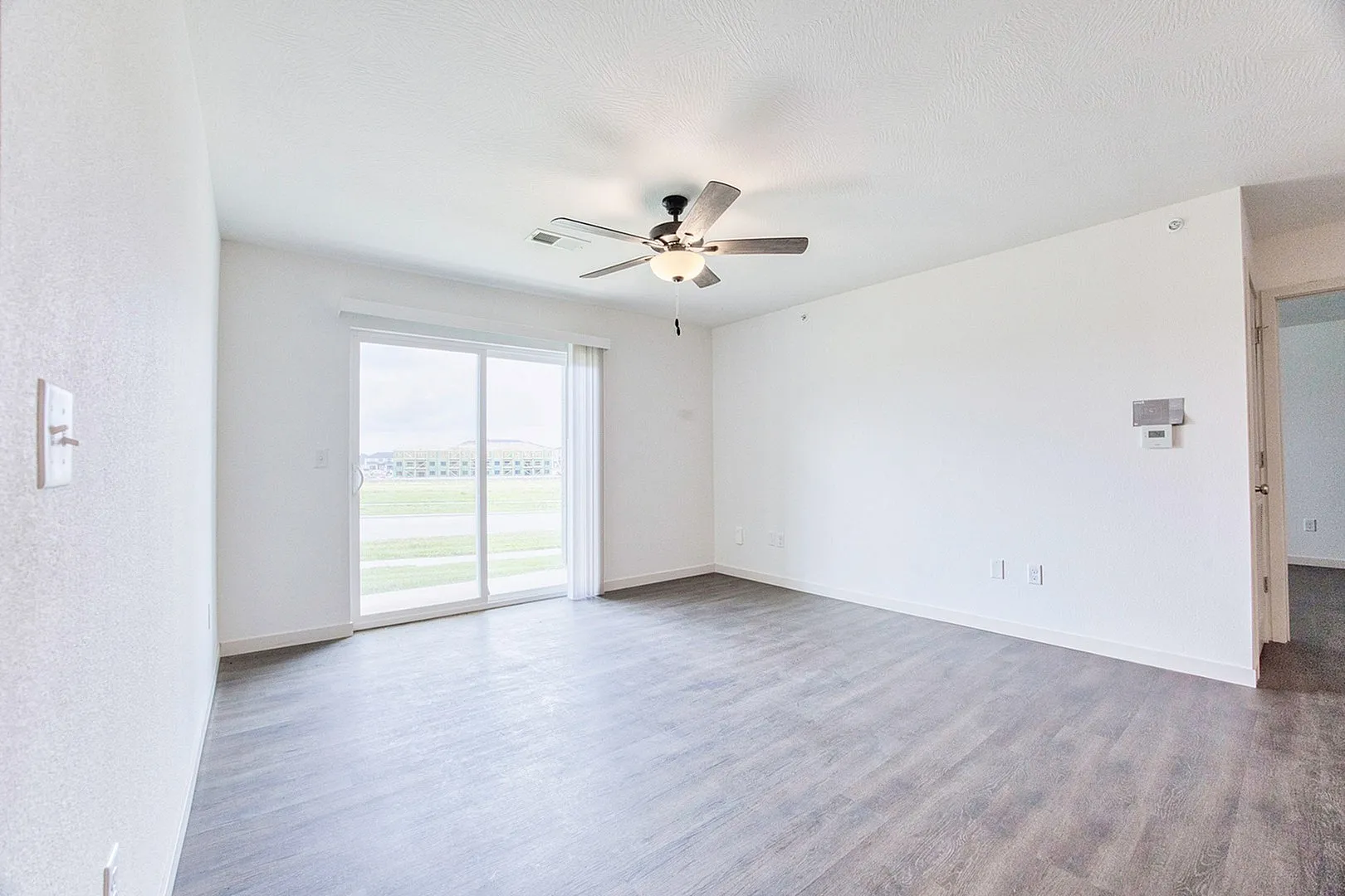 Bright and airy living room with elegant ceiling fan, sleek hardwood flooring, and expansive sliding glass doors leading to a serene outdoor view.