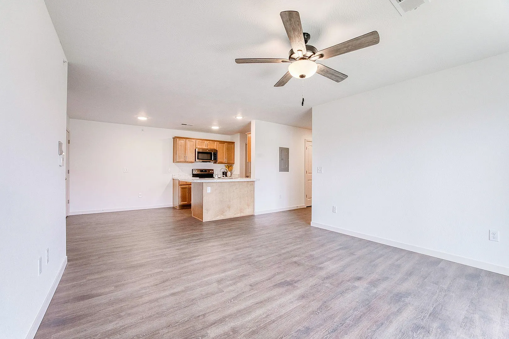 Bright and spacious open-concept living area with elegant wood flooring, modern ceiling fan, and a cozy kitchen featuring sleek appliances and wooden cabinetry.