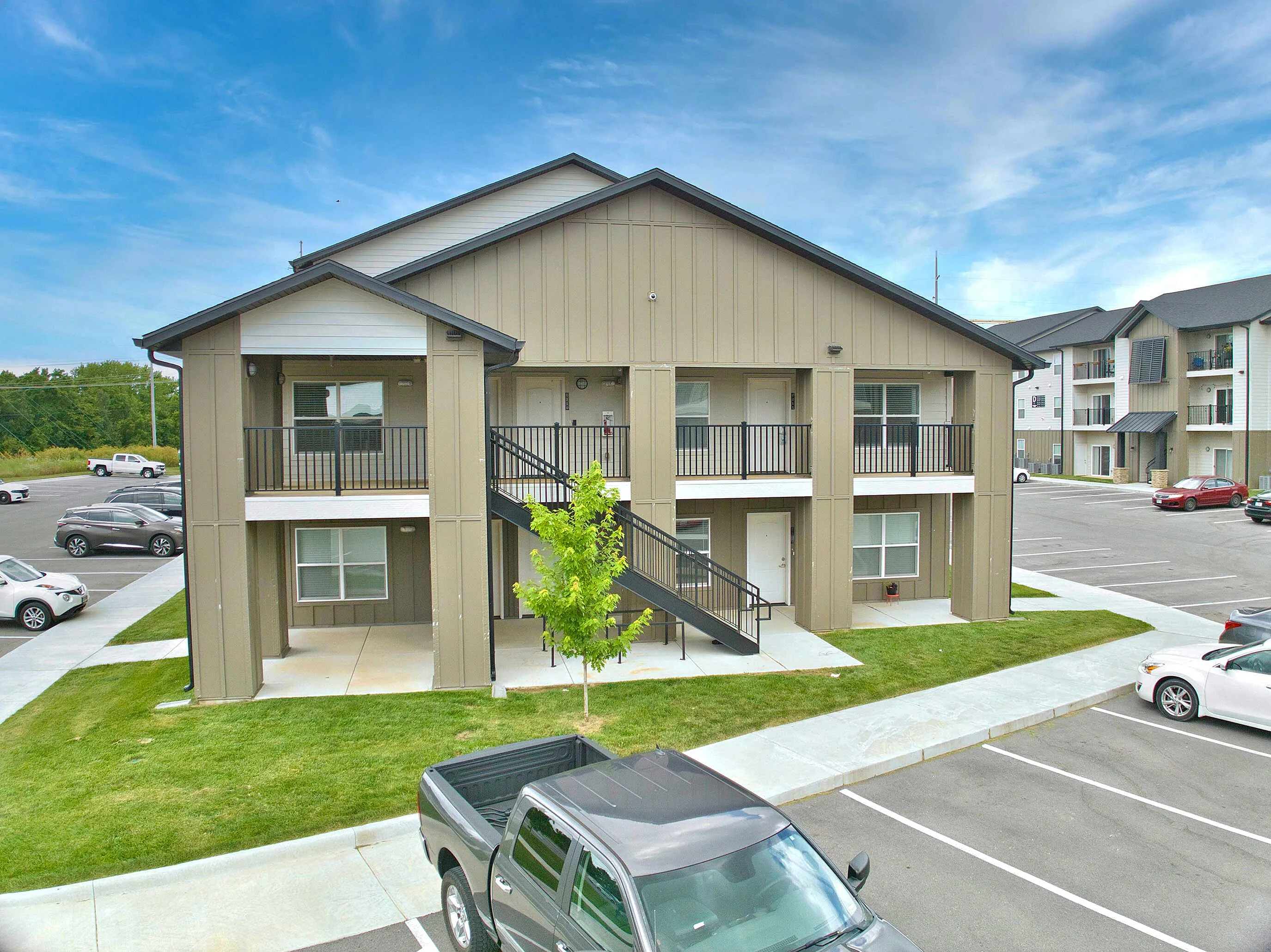 Modern two-story apartment building with ample parking spaces and well-maintained green lawn under a clear blue sky.