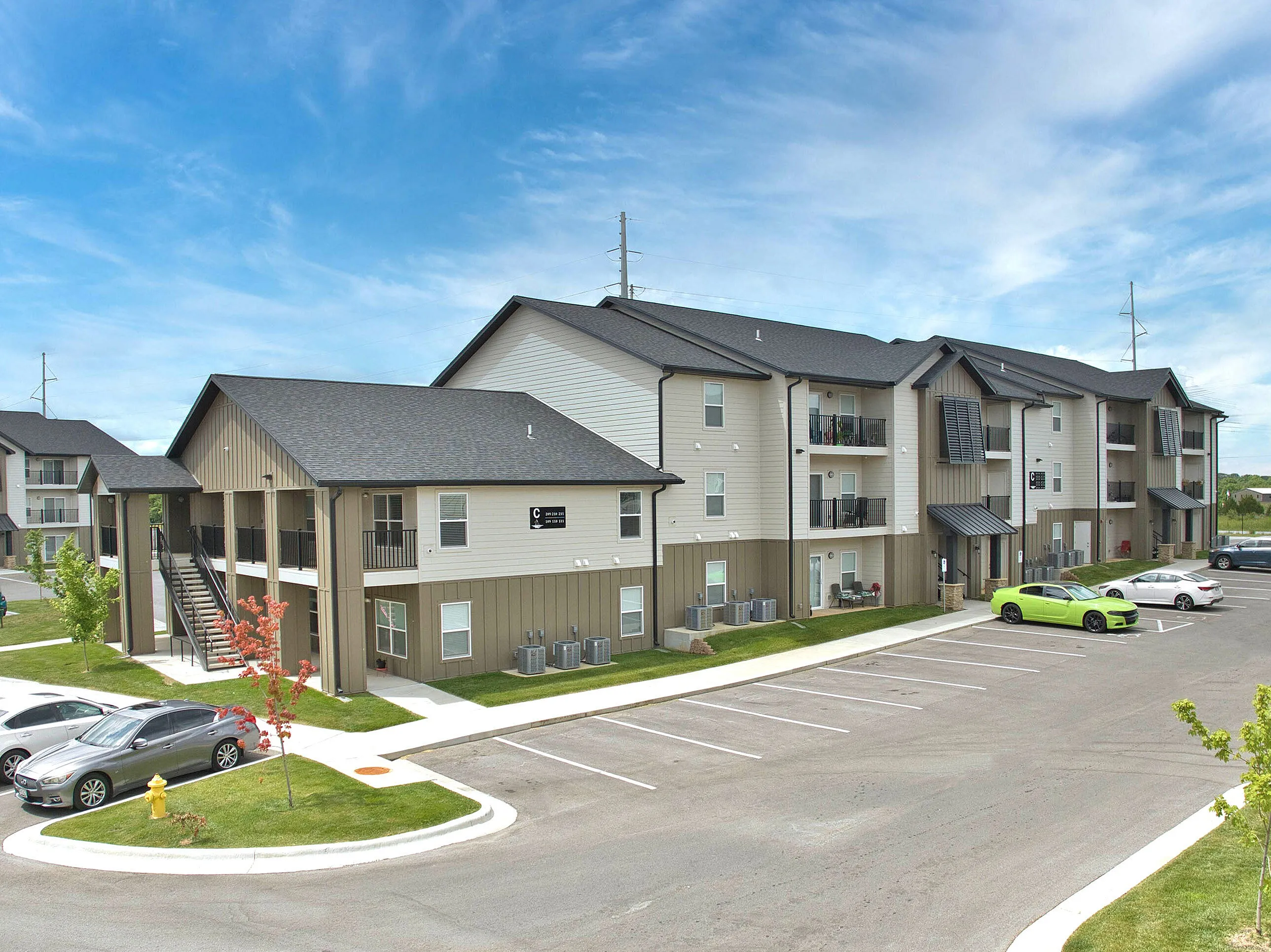 Modern apartment complex featuring spacious balconies, ample parking, and well-maintained landscaping under a bright blue sky.