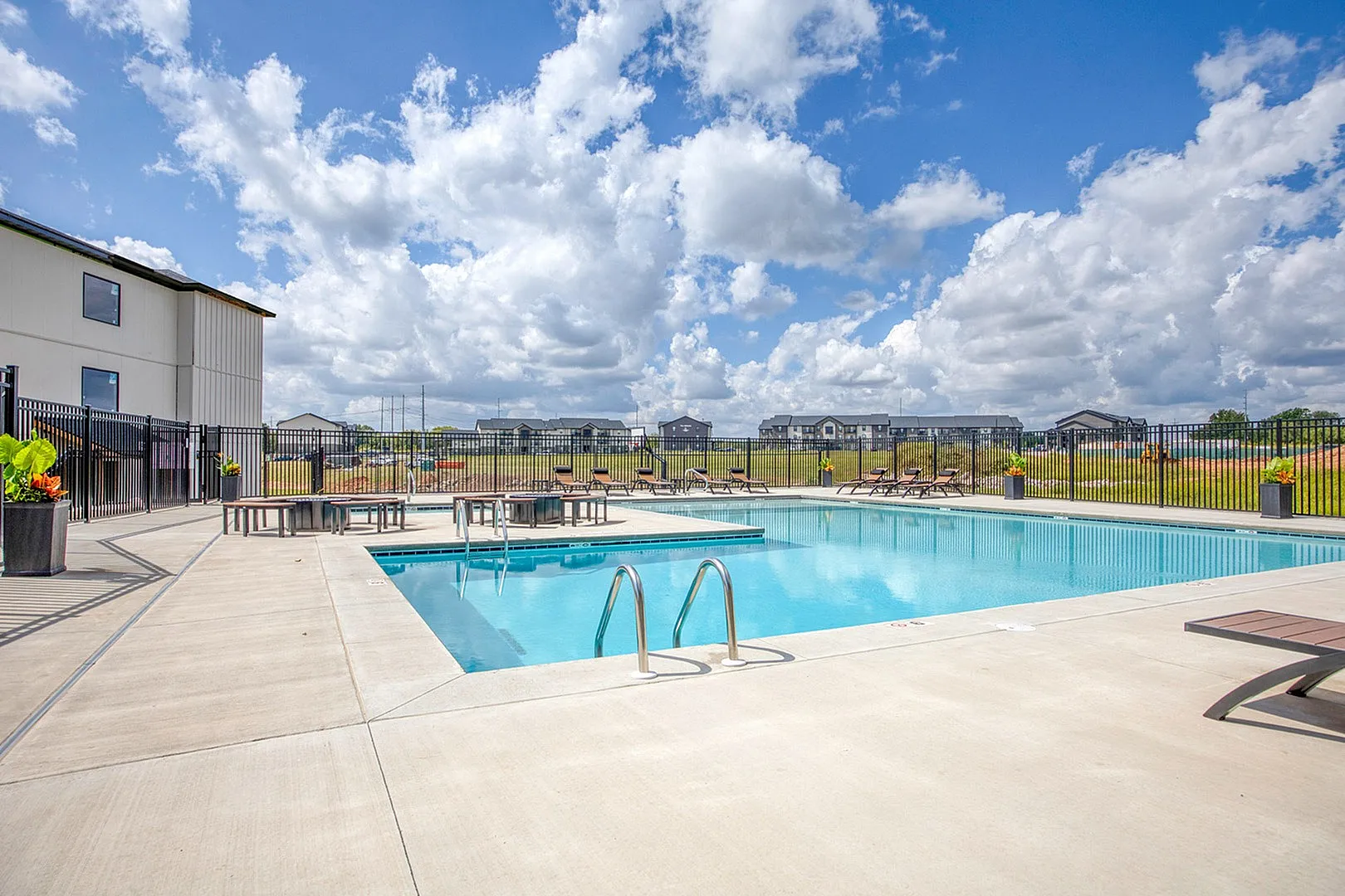 Inviting outdoor pool area with modern lounge chairs and vibrant planters, perfect for relaxation under a beautiful blue sky.