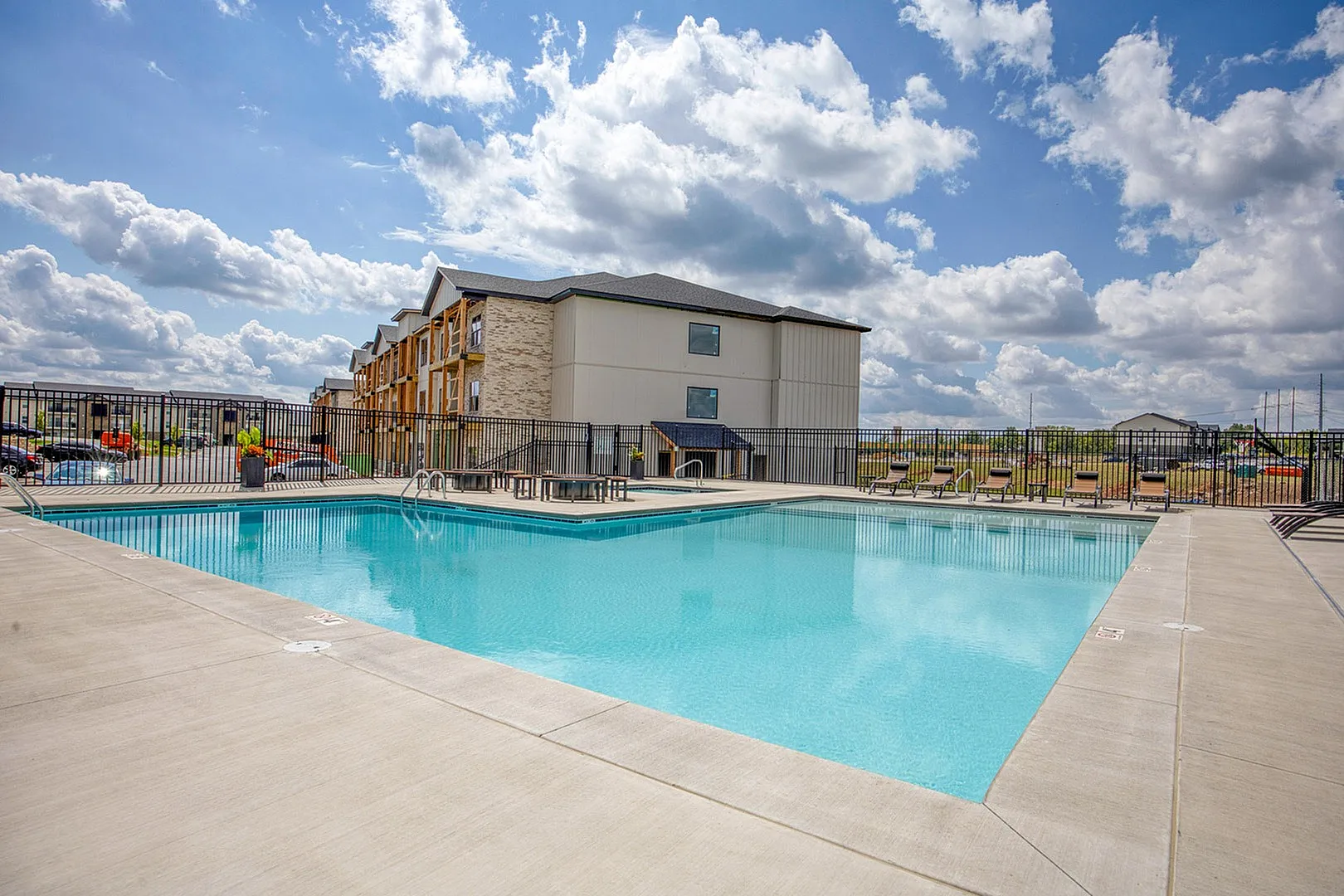 Inviting swimming pool area with modern seating at a stylish apartment complex, under a beautiful sky.